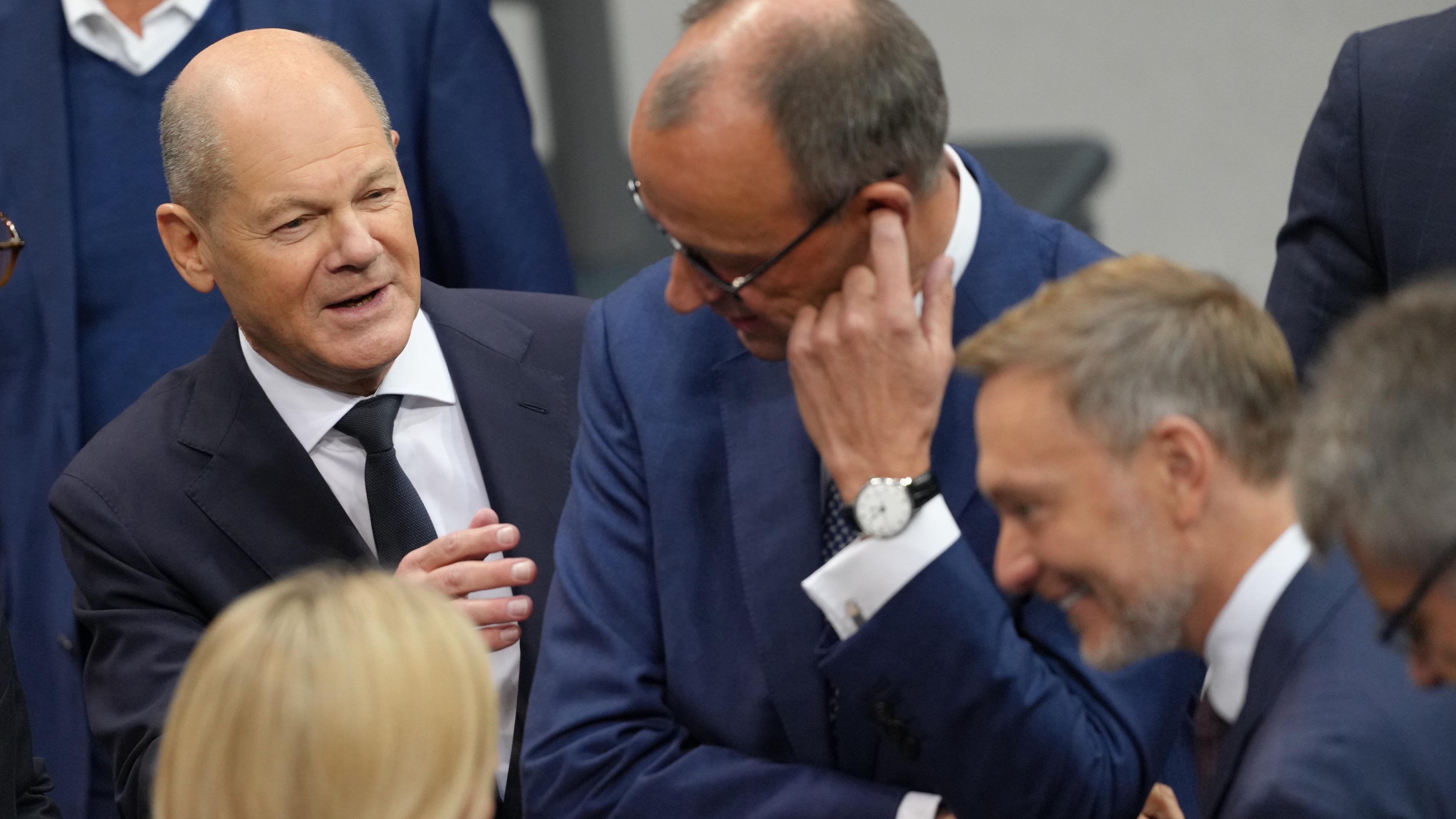 Bundeskanzler Olaf Scholz (SPD, l) spricht im Plenum des Bundestags vor seiner Regierungserklärung mit Friedrich Merz (M)