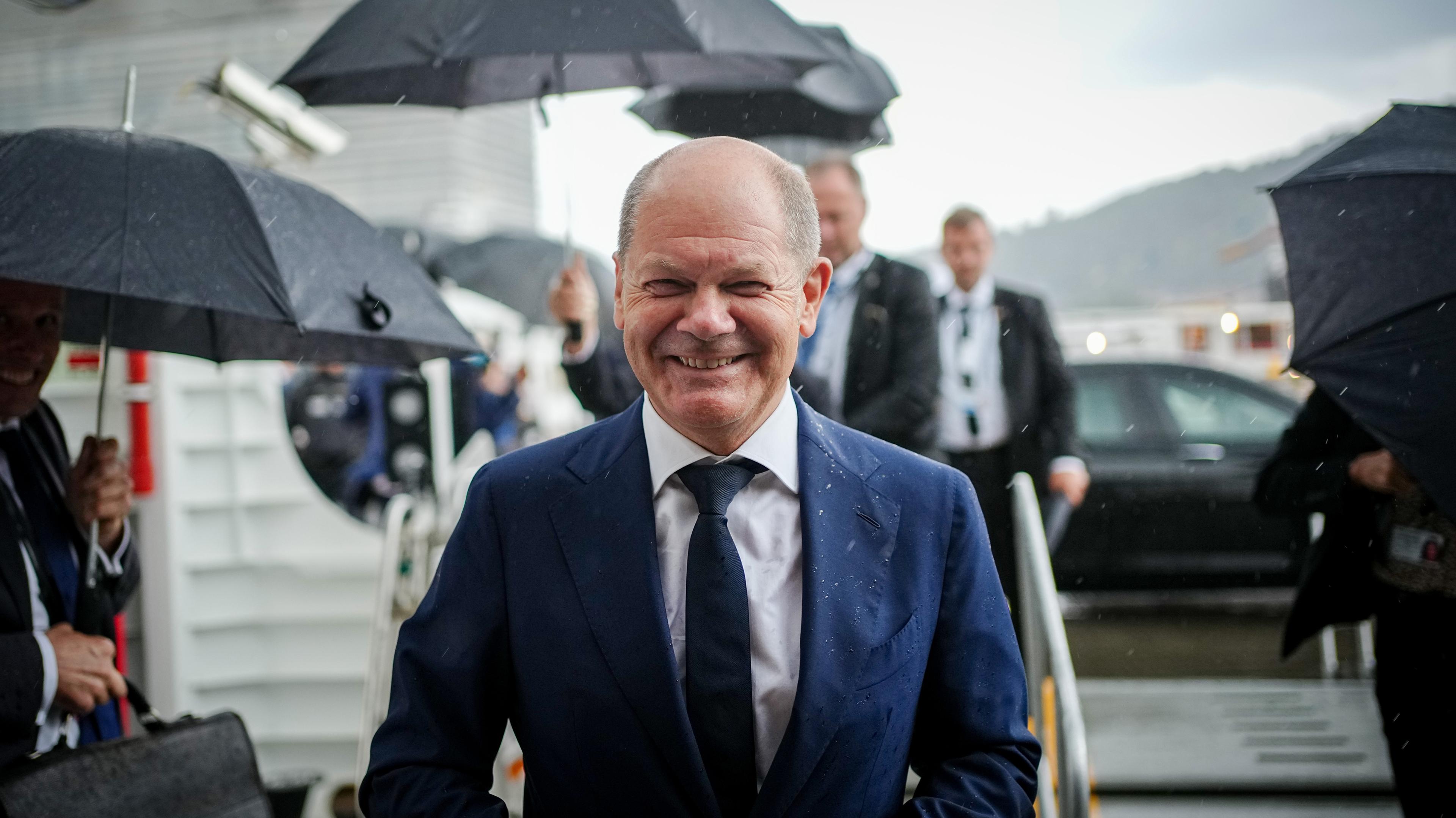 Bundeskanzler Olaf Scholz steh im Regen und lächelt