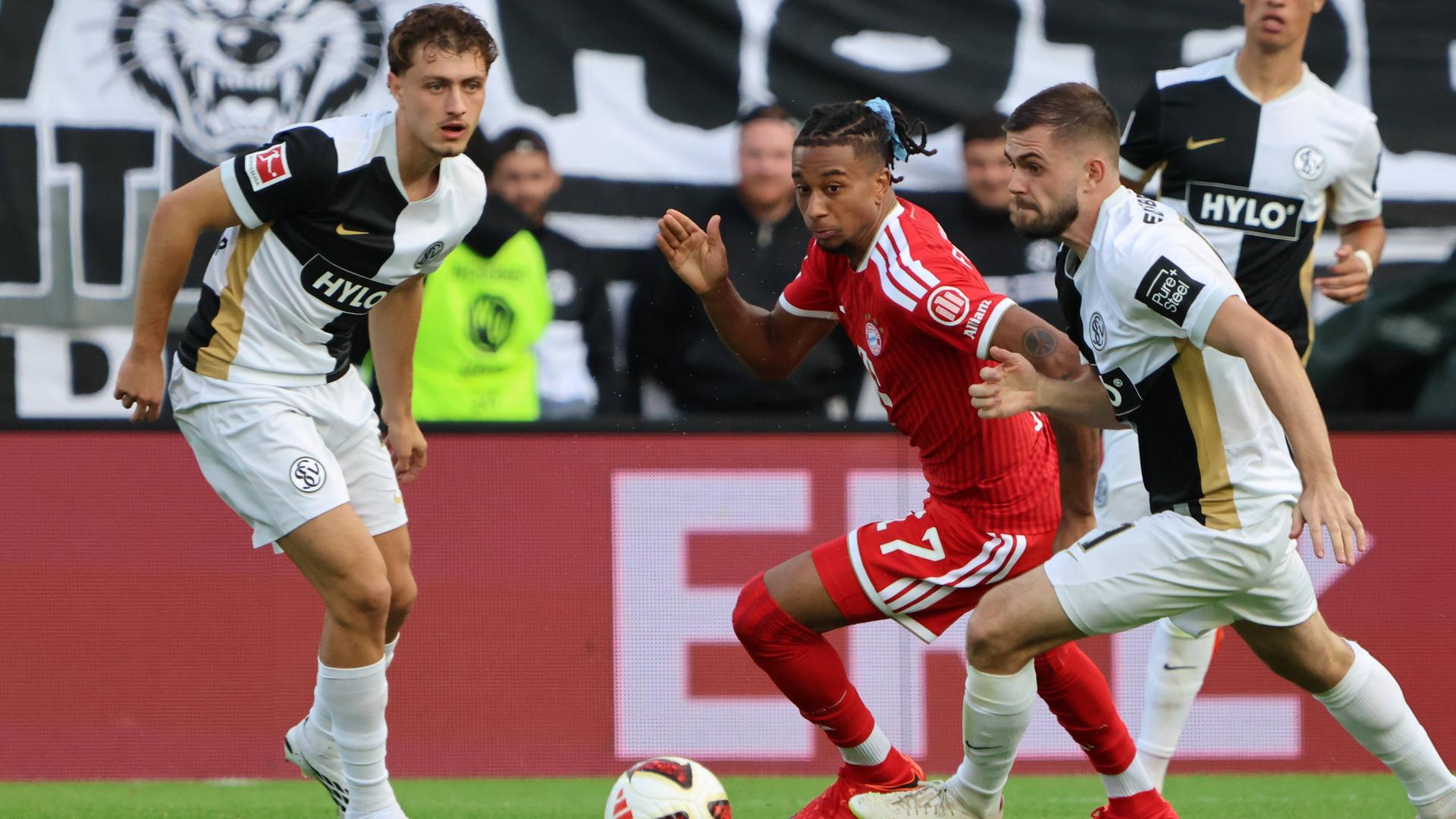 Bayerns Flügelspieler Michael Olise wird von seinen beiden Elversberger Kontrahenten Maurice Krattenmacher und Lukasz Poreba bedrängt