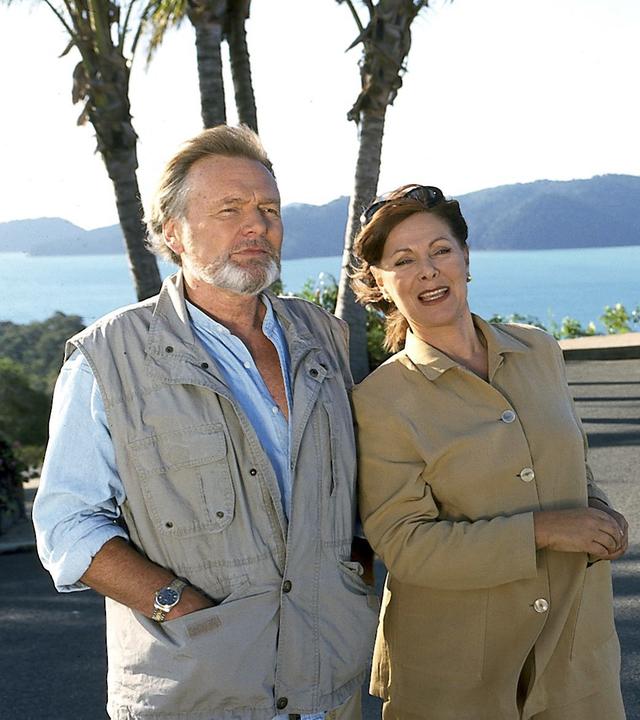"Das Traumschiff: Olympia 2000": Beatrice (Heide Keller) und Herbert Ernst (Helmut Griem) stehen nebeneinander und blicken nach vorne. Im Hintergrund ist das Meer zu sehen und ein Pavillon.