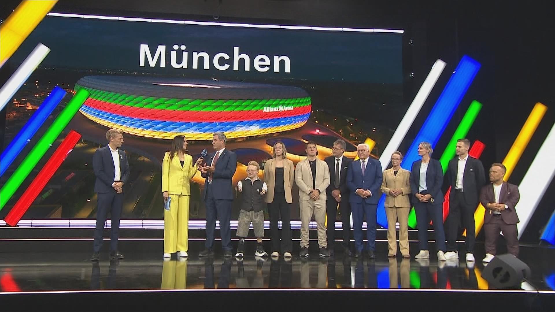 Auf der Bühne wird verkündet, dass München sich als Austragungsort für Olympia bewirbt.
