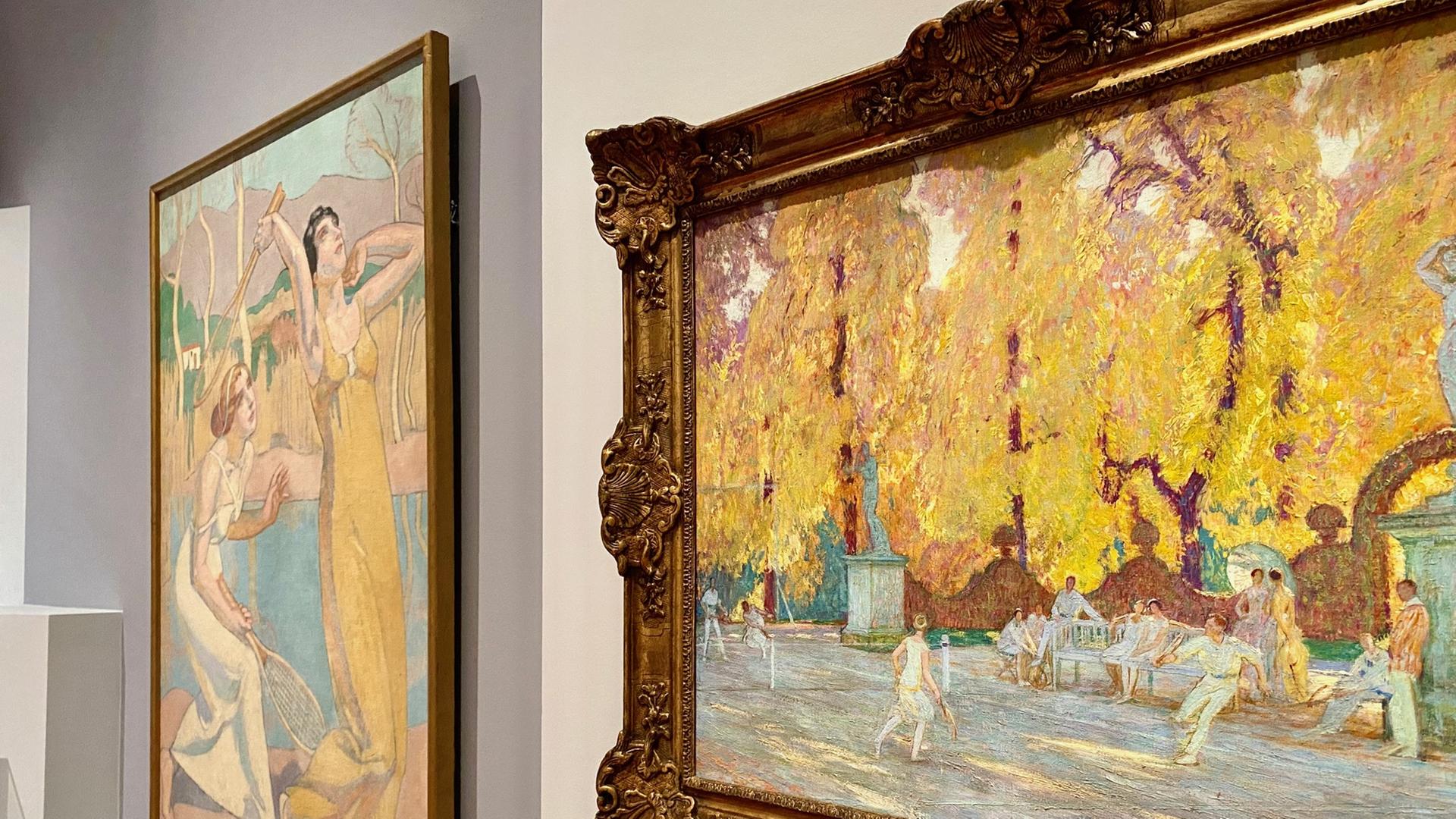 Zwei Gemälde hängen in einer Gallerie. Sie zeigen Menschen beim Tennis spielen in der Sonne. Der vordere Bilderrahmen ist massiv und gold, der hintere ist schlicht gehalten.