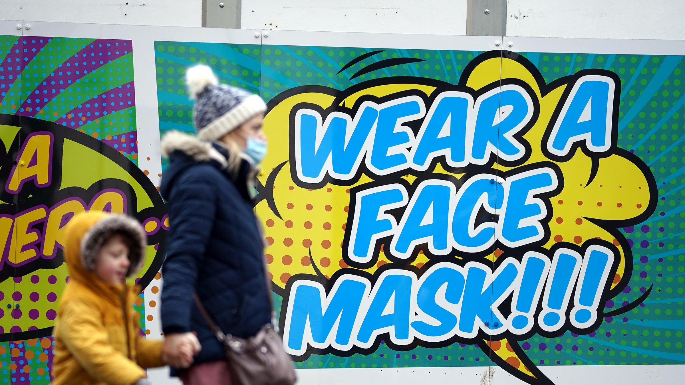 Frau geht mit ihrem Kind an einem Plakat im Stadtzentrum von Nottingham vorbei, das zum Tragen einer Mund-Nasen-Bedeckung auffordert