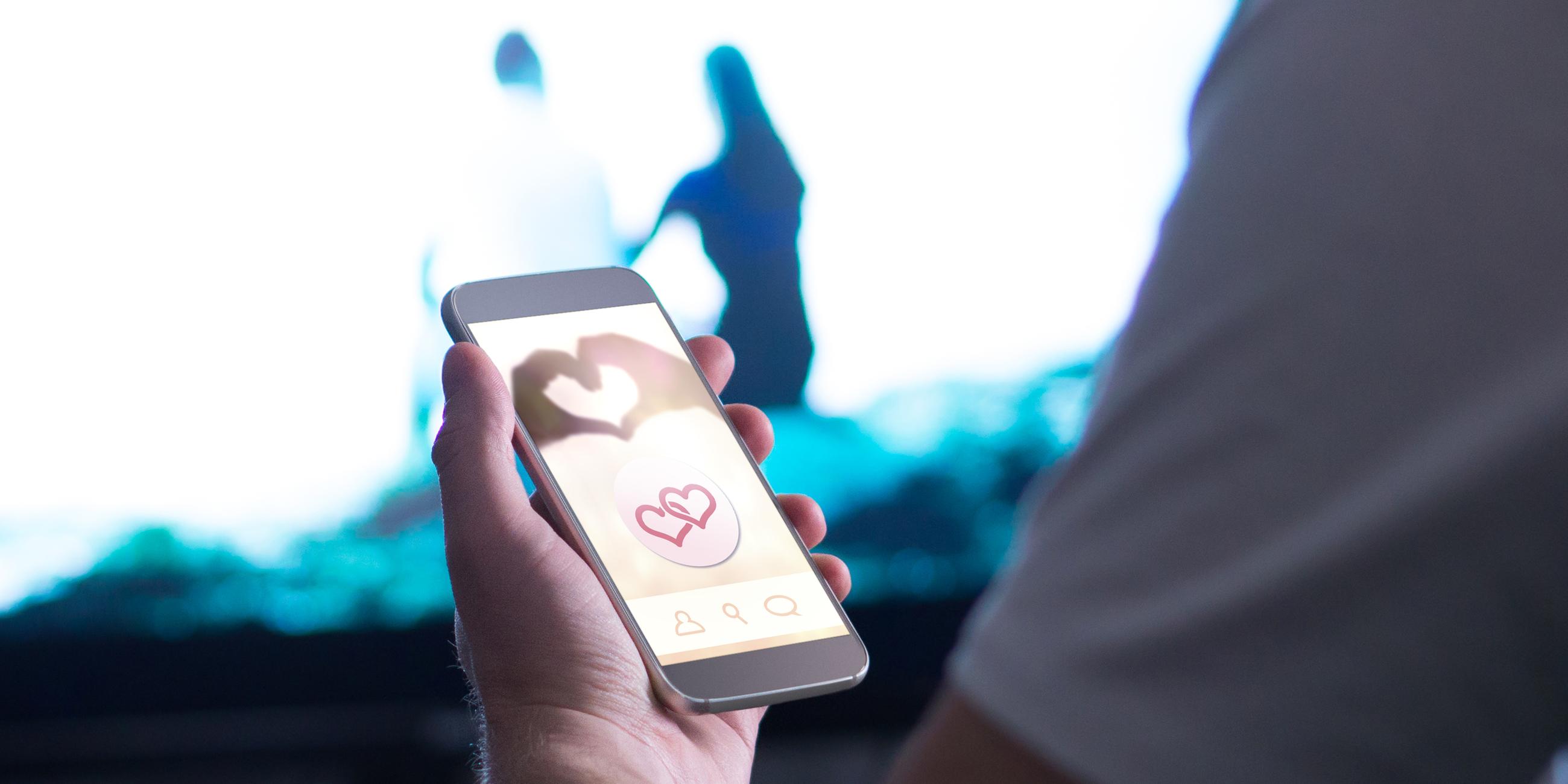 Ein Mann hält ein Smartphone in seiner linken Hand, auf dem eine Dating-App geöffnet ist.
