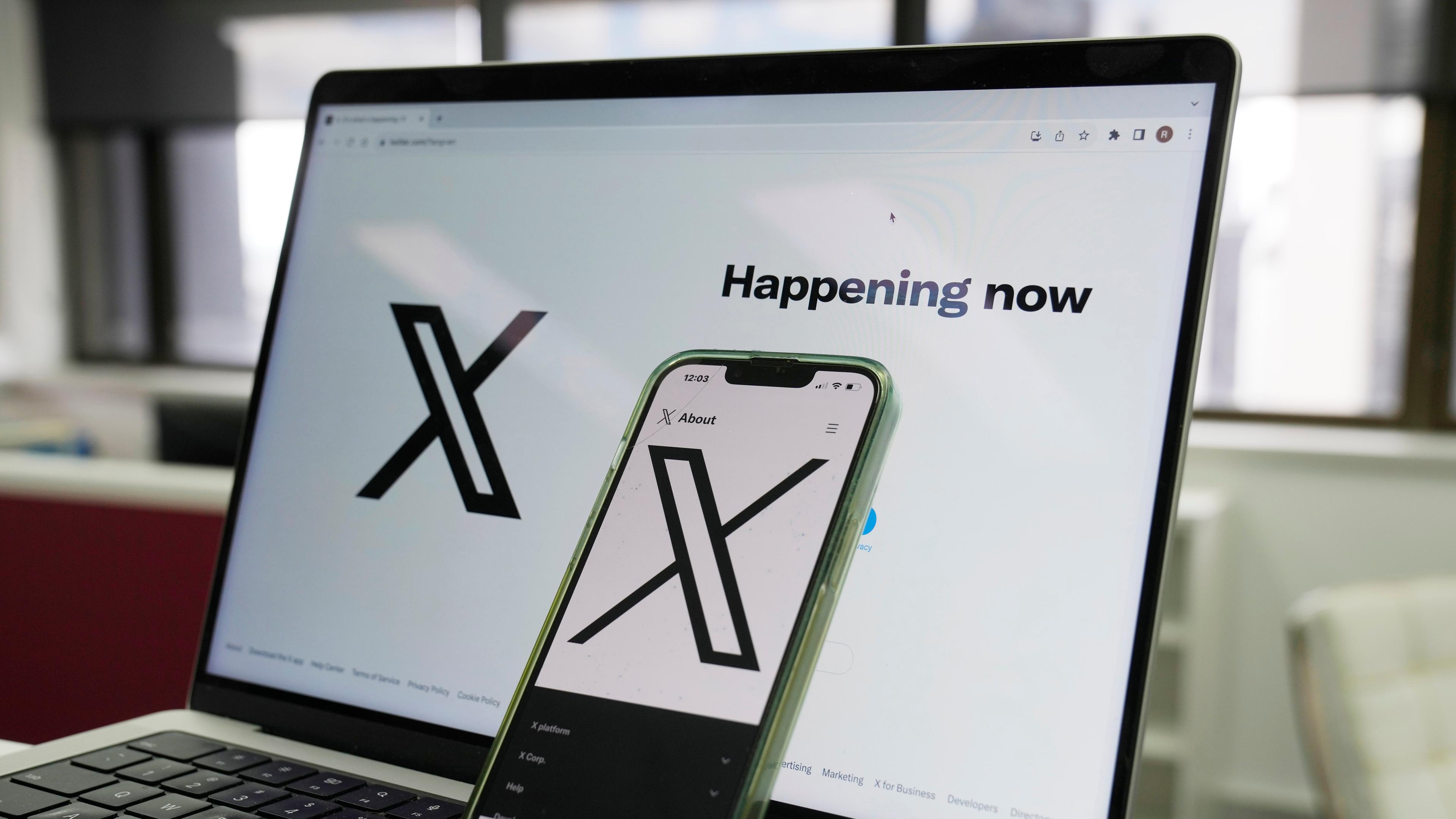 Ein Smartphone steht auf der Tastatur eines Laptops, beide zeigen das Logo der Online-Plattform X (ehemals Twitter)
