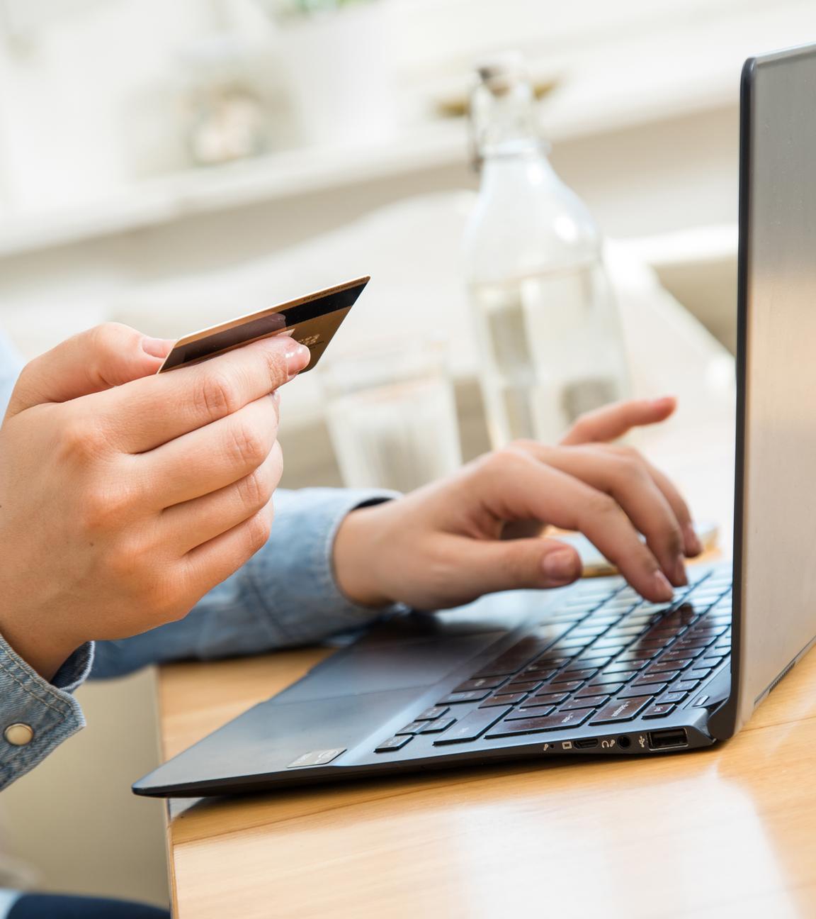 Eine Frau hält ihre Kreditkarte, während sie an ihrem Laptop Online-Einkäufe tätigt.