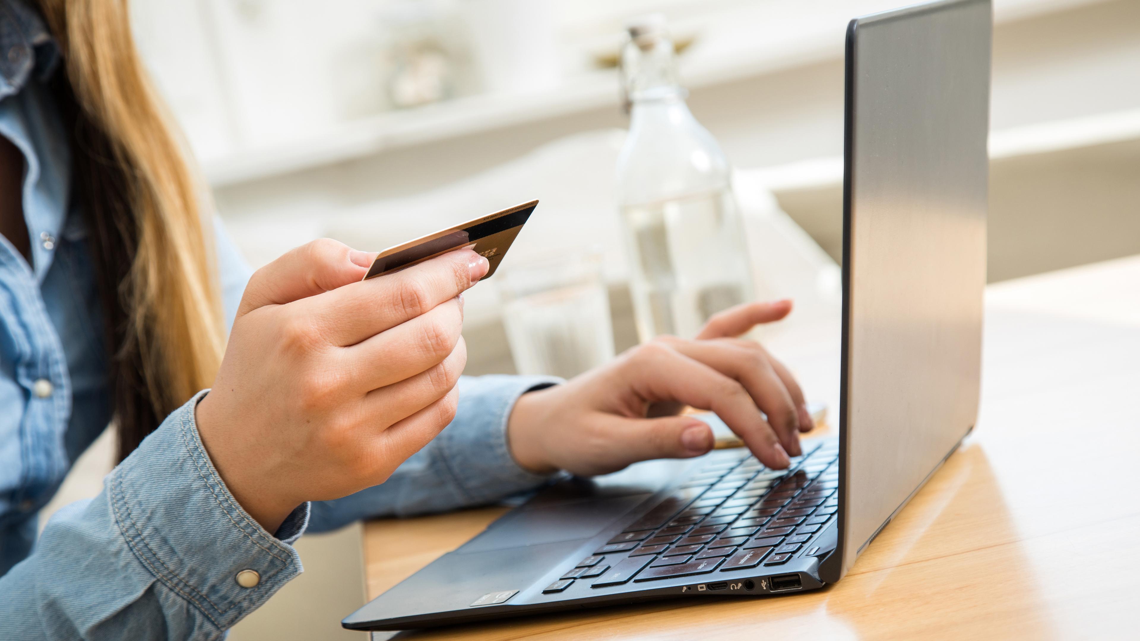 Eine Frau hält ihre Kreditkarte, während sie an ihrem Laptop Online-Einkäufe tätigt.