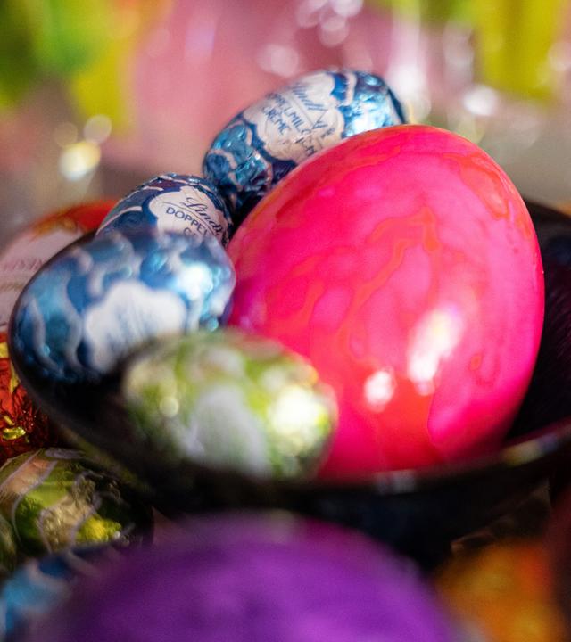 Ostereier und Schokoeier liegen in Schalen und auf einem Tisch.
