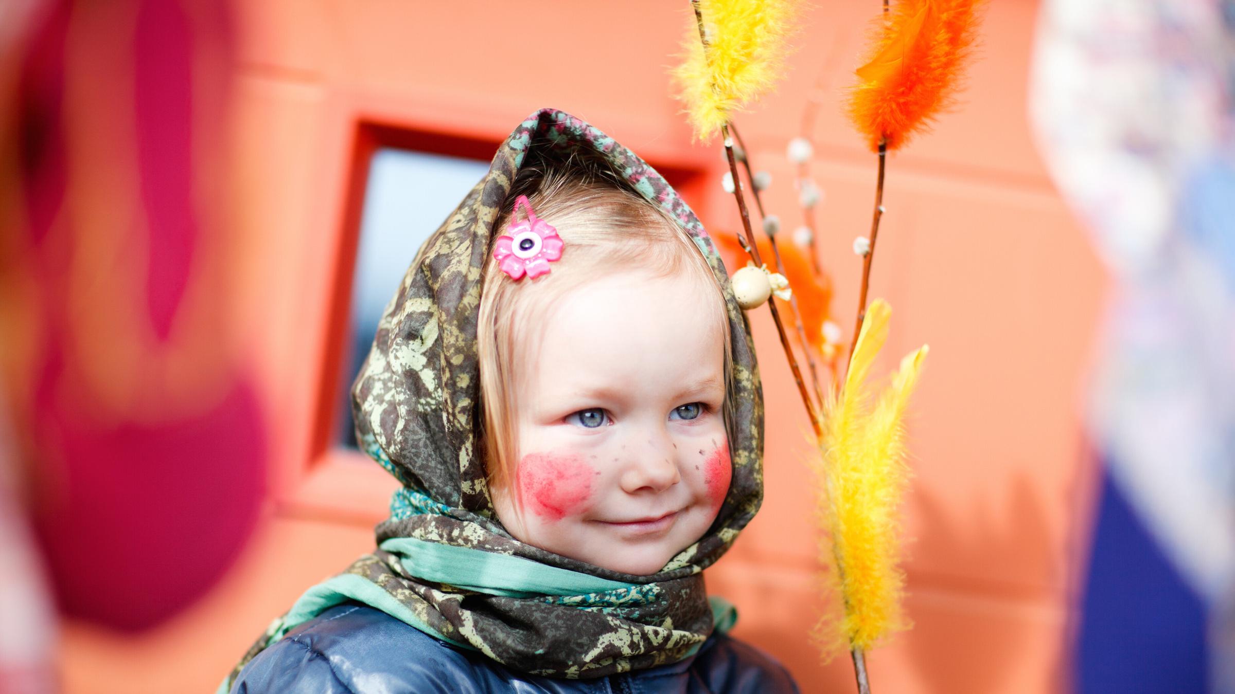 kleines Mädchen ist als Hexe verkleidet und hält bunten Weidenzweig