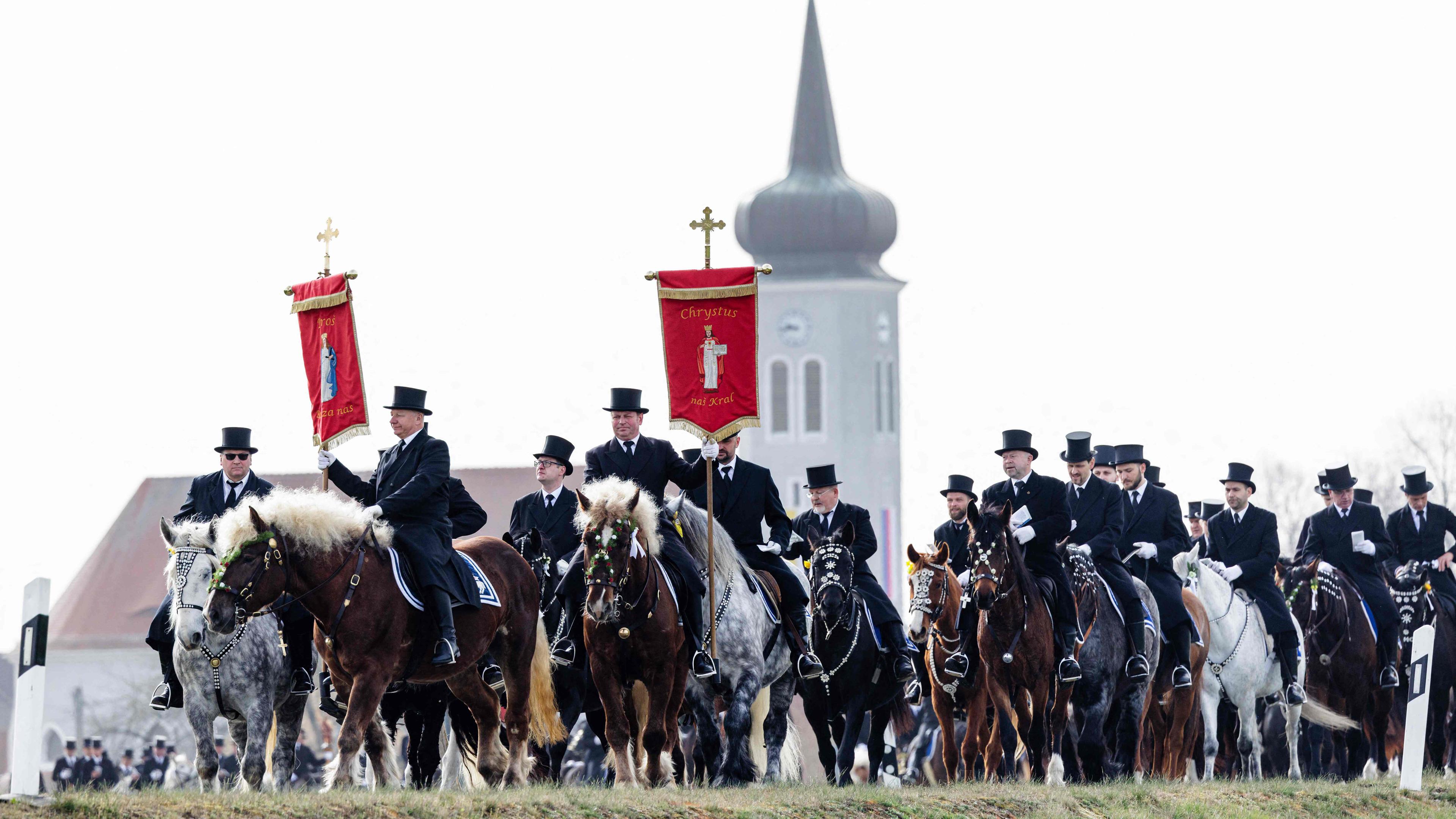 Sorbische Reiter in schwarzer Tracht singen, während sie während der sorbischen Osterprozession am Ostersonntag, dem 31.03.2024, in Ralbitz, Ostdeutschland, reiten.