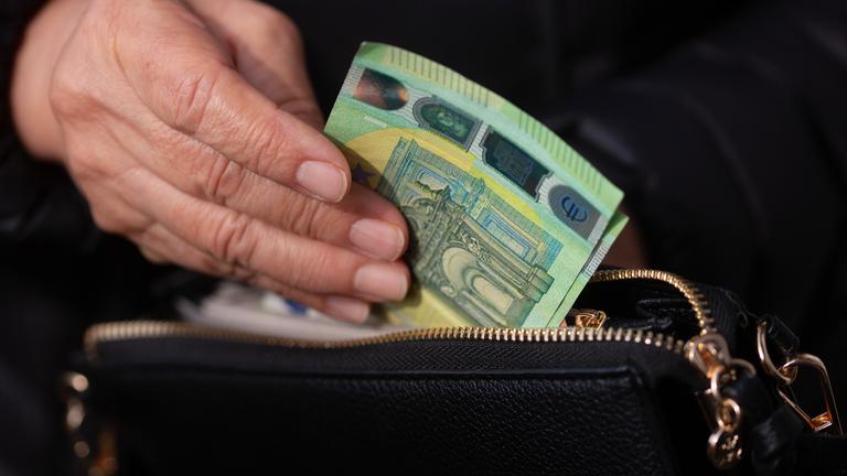 Eine Seniorin steckt Euro-Banknoten in eine Geldbörse. 