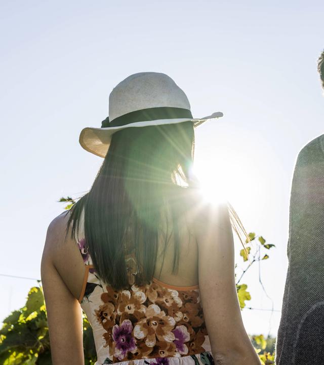 Eine junge Frau mit Sonnenhut und ein Mann laufen Händchenhaltend an einem sonnigen Tag im Grünen.