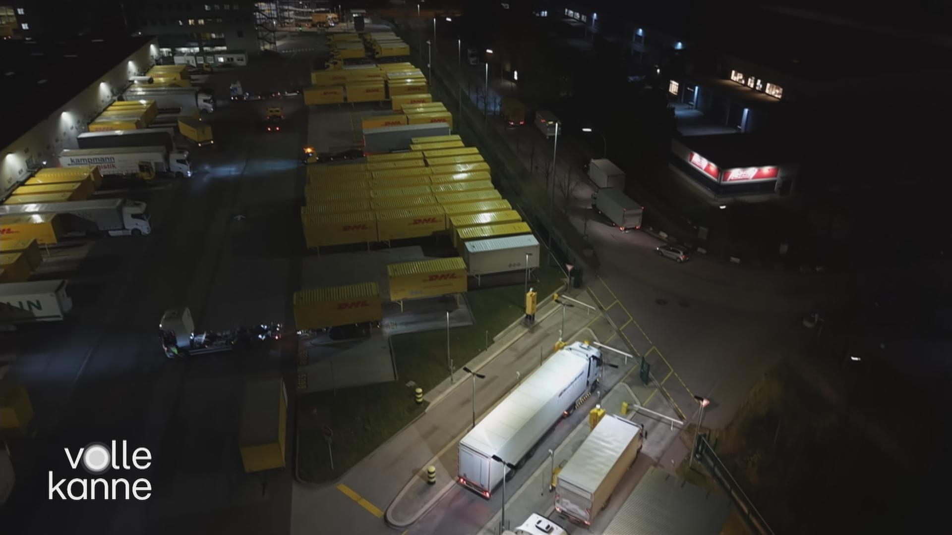 Der Parkplatz eines Paketzentrums ist zu sehen. Der Parkplatz ist voll mit LKWs. 