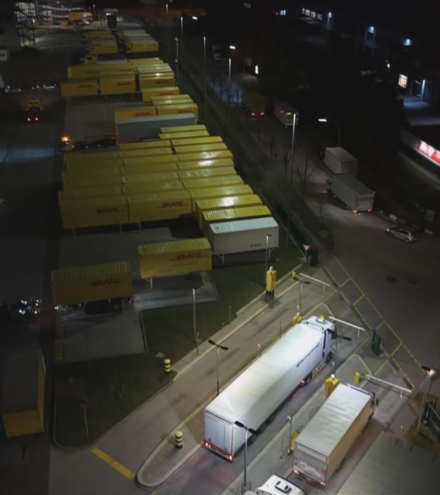 Der Parkplatz eines Paketzentrums ist zu sehen. Der Parkplatz ist voll mit LKWs. 