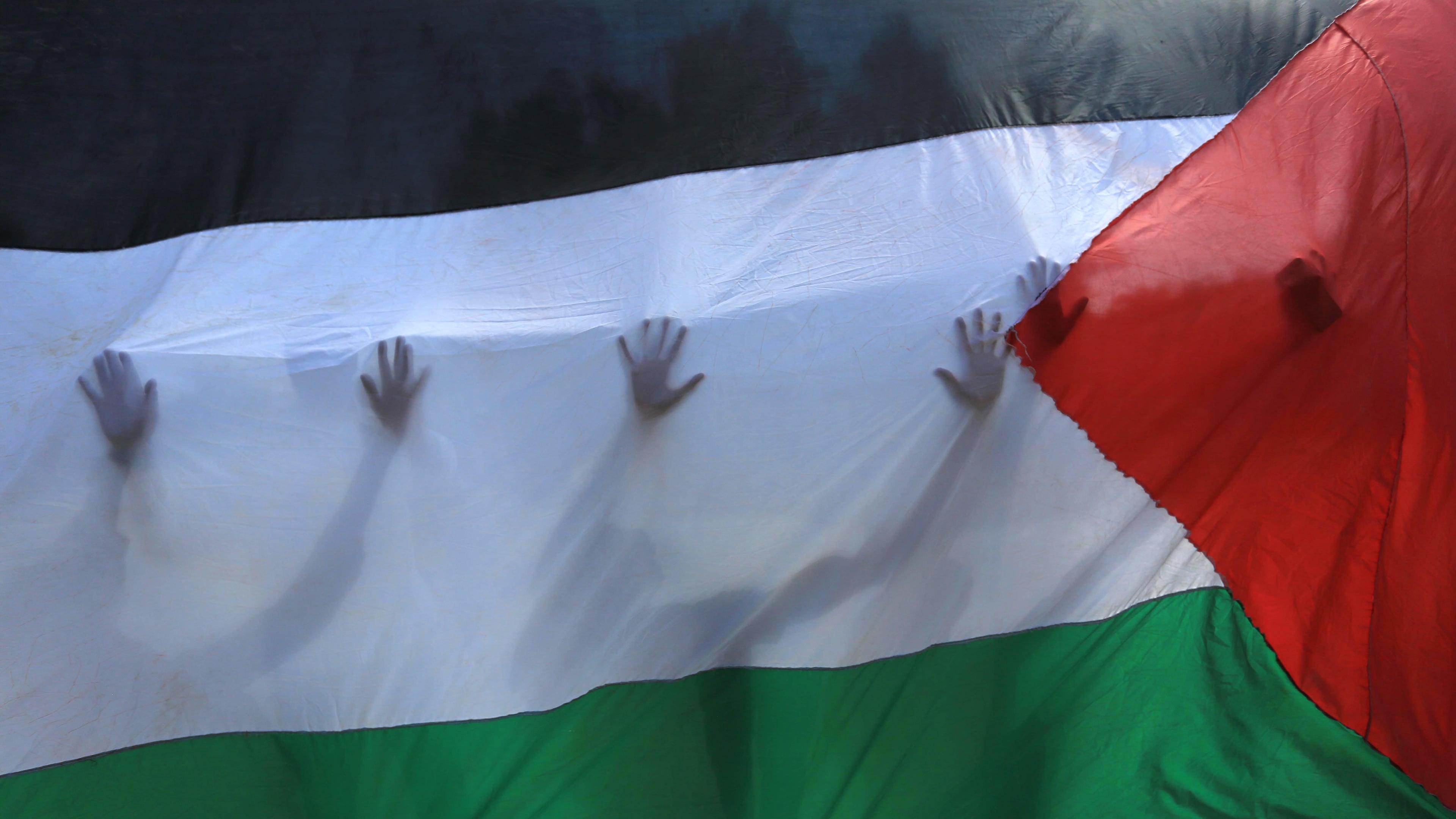 Palästinensische Freiwillige stehen hinter einer palästinensischen Fahne, durch die ihre Silhouetten zu erkennen sind.
