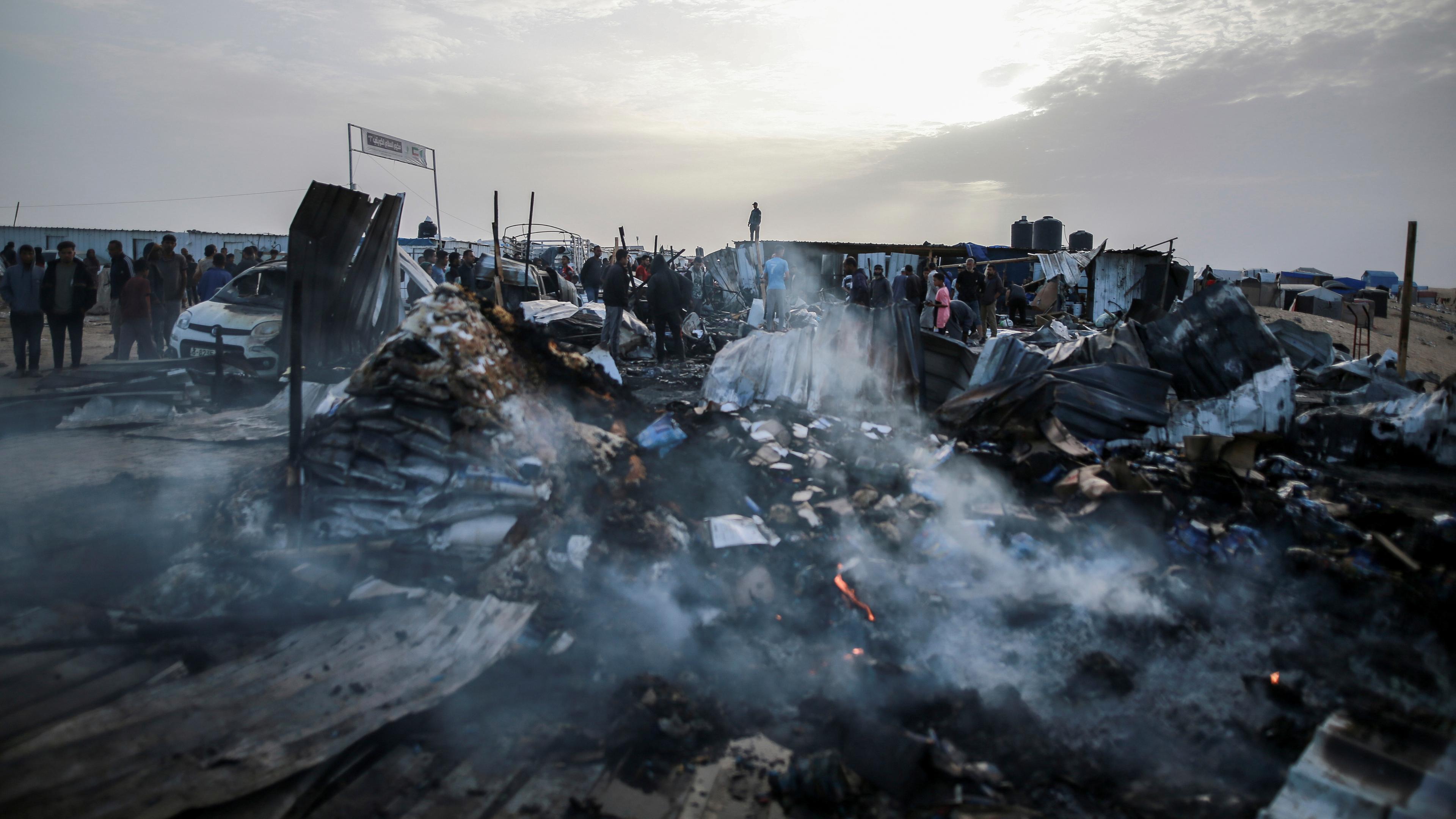 Palästinensische Gebiete, Rafah: Palästinenser inspizieren zerstörte Zelte und Unterkünfte neben einem ausgebrannten Auto nach einem israelischen Luftangriff auf ein Flüchtlingslager.