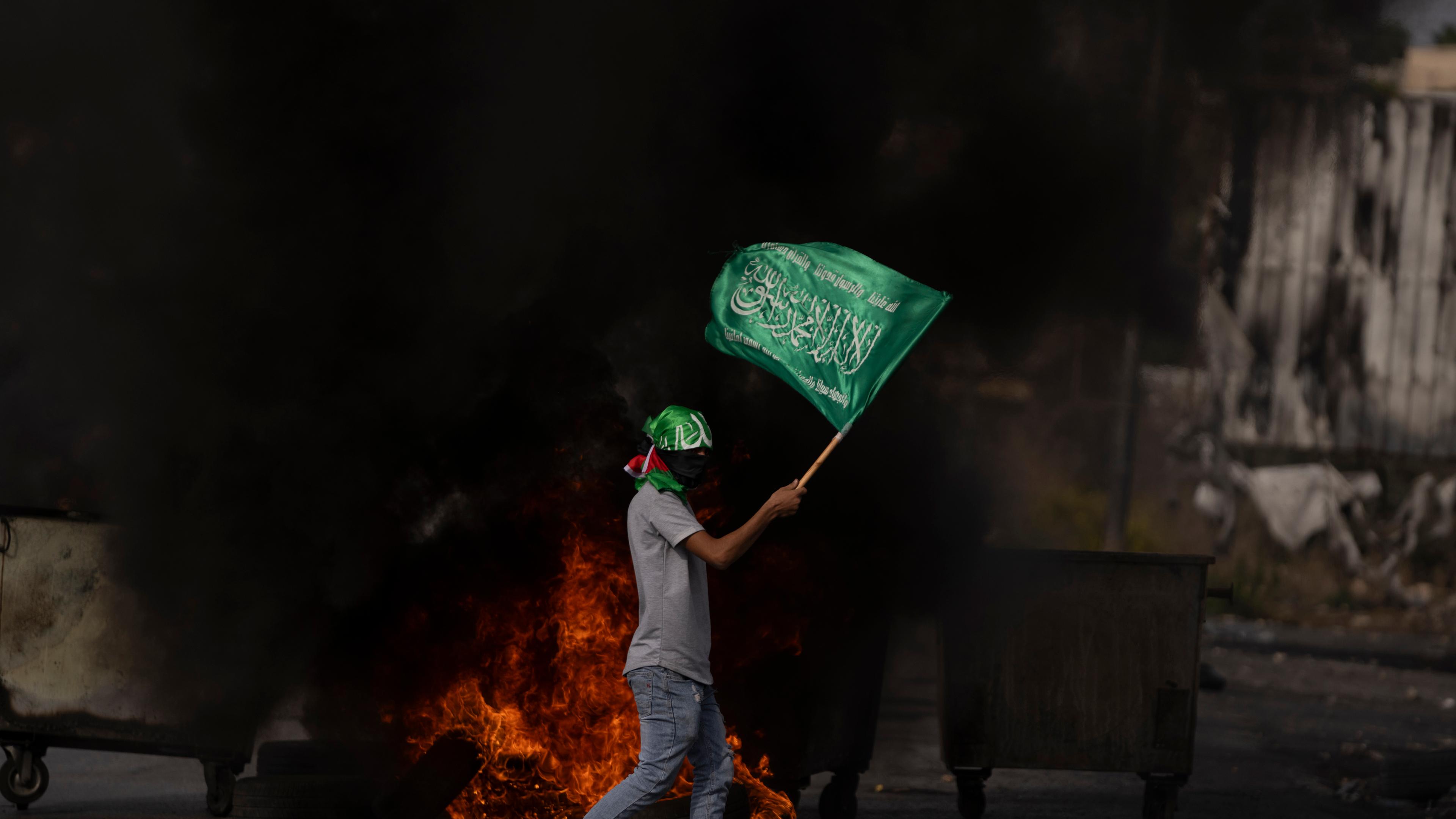 Ein palästinensischer Demonstrant mit einer Hamas-Flagge hinter brennenden Reifen in der Stadt Ramallah im Westjordanland