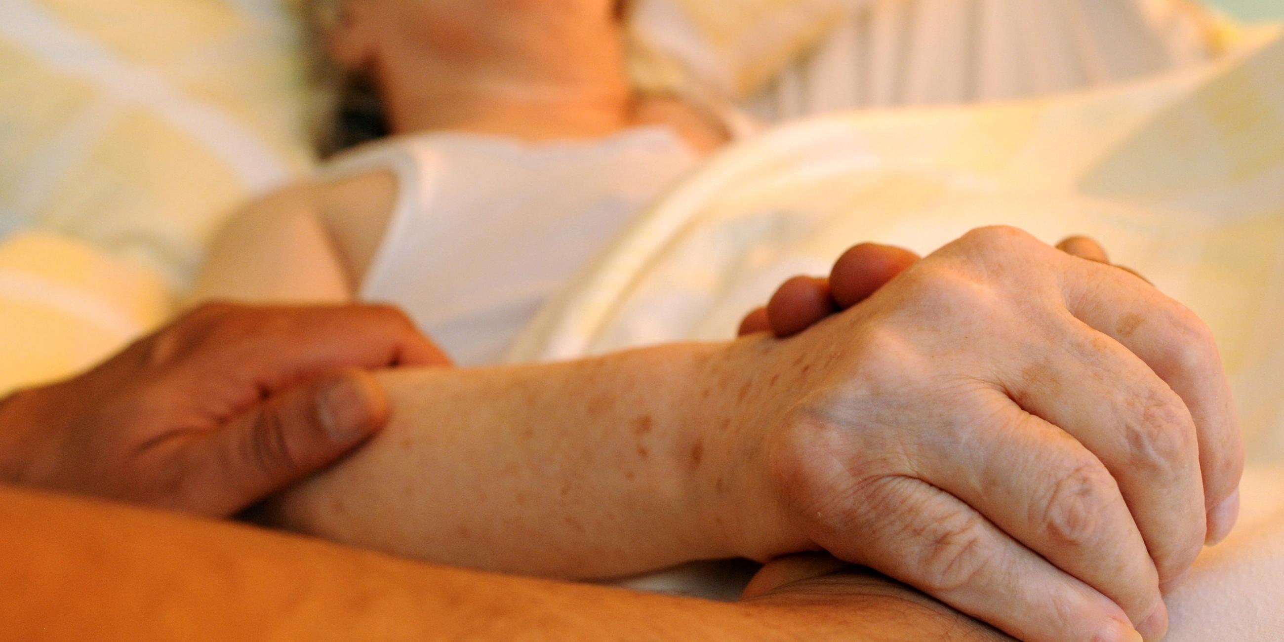 Ein Pfleger hält die Hand einer pflegebedürftigen Frau
