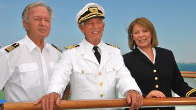 Zusammen mit Beatrice (Heide Keller) und Dr. Schröder (Horst Naumann) steht Kapitän Paulsen (Siegfried Rauch) an Deck des Traumschiffs und sie blicken in die Ferne.