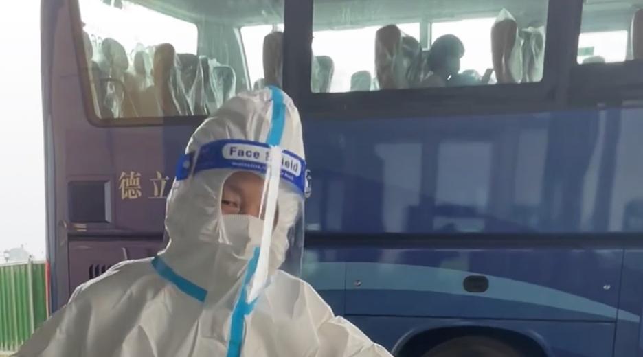Zu sehen ist ein Person in einem weißen Schutzanzug vor einem Bus. Sie hält eine Tüte in Essen und scheint unter der Maske zu lächeln. 