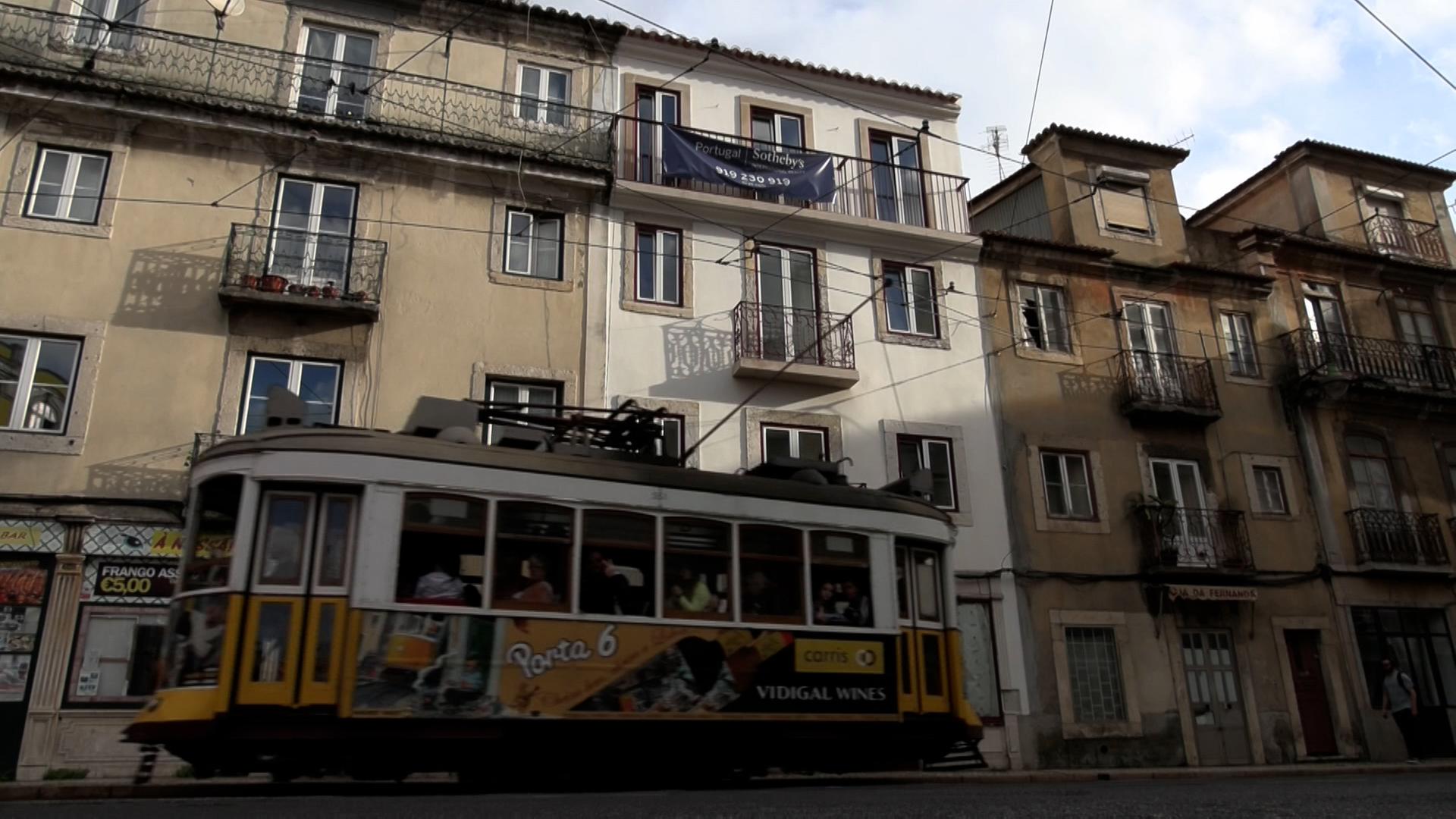 Eine klassisch gelb-weiße Tram fährt durch die Straßen von Lissabon.