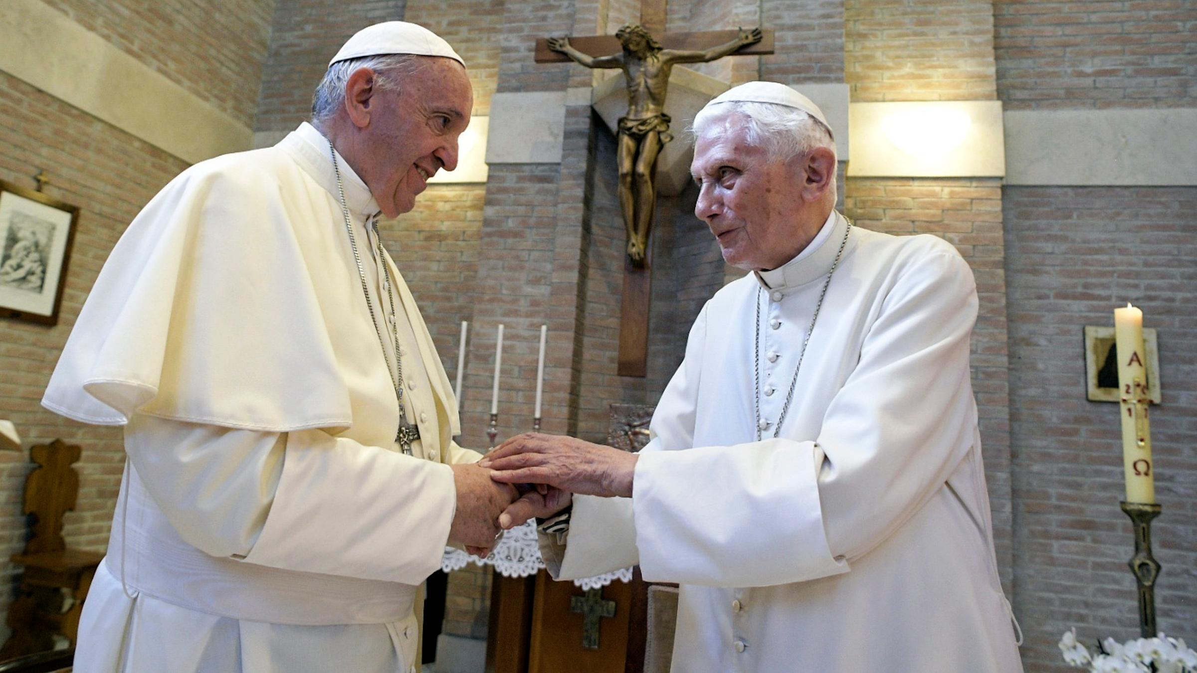 Papst Benedikt und Papst Franziskus geben sich die Hand. 