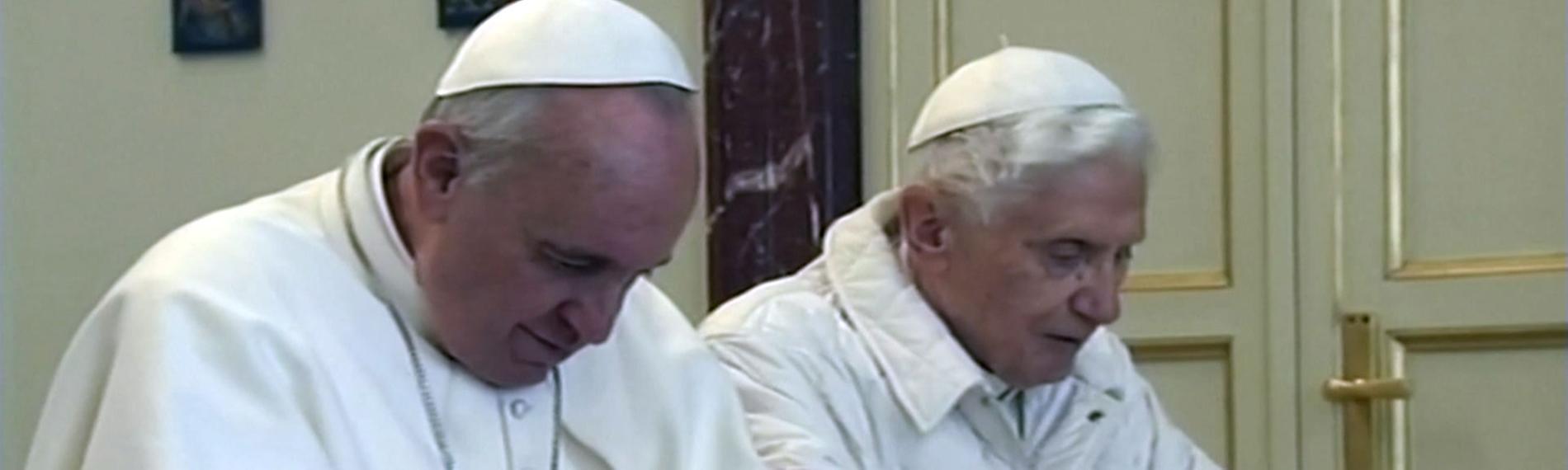 Papst Benedikt XVI. und Papst Franziskus kniend beim Gebet und haben beide weiße Gewänder an