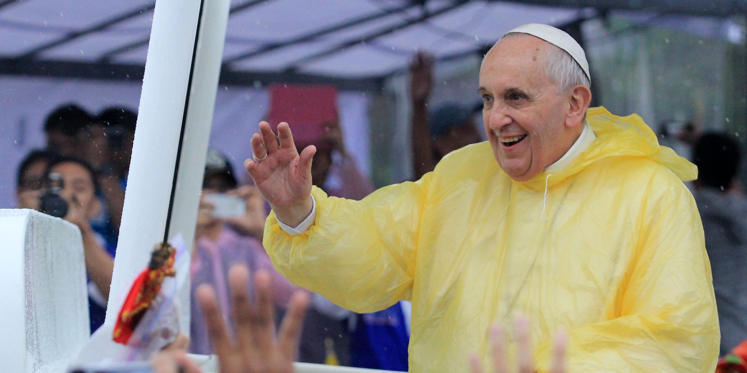  Papst Franziskus steht lachend im Papamobil und winkt Menschen zu.