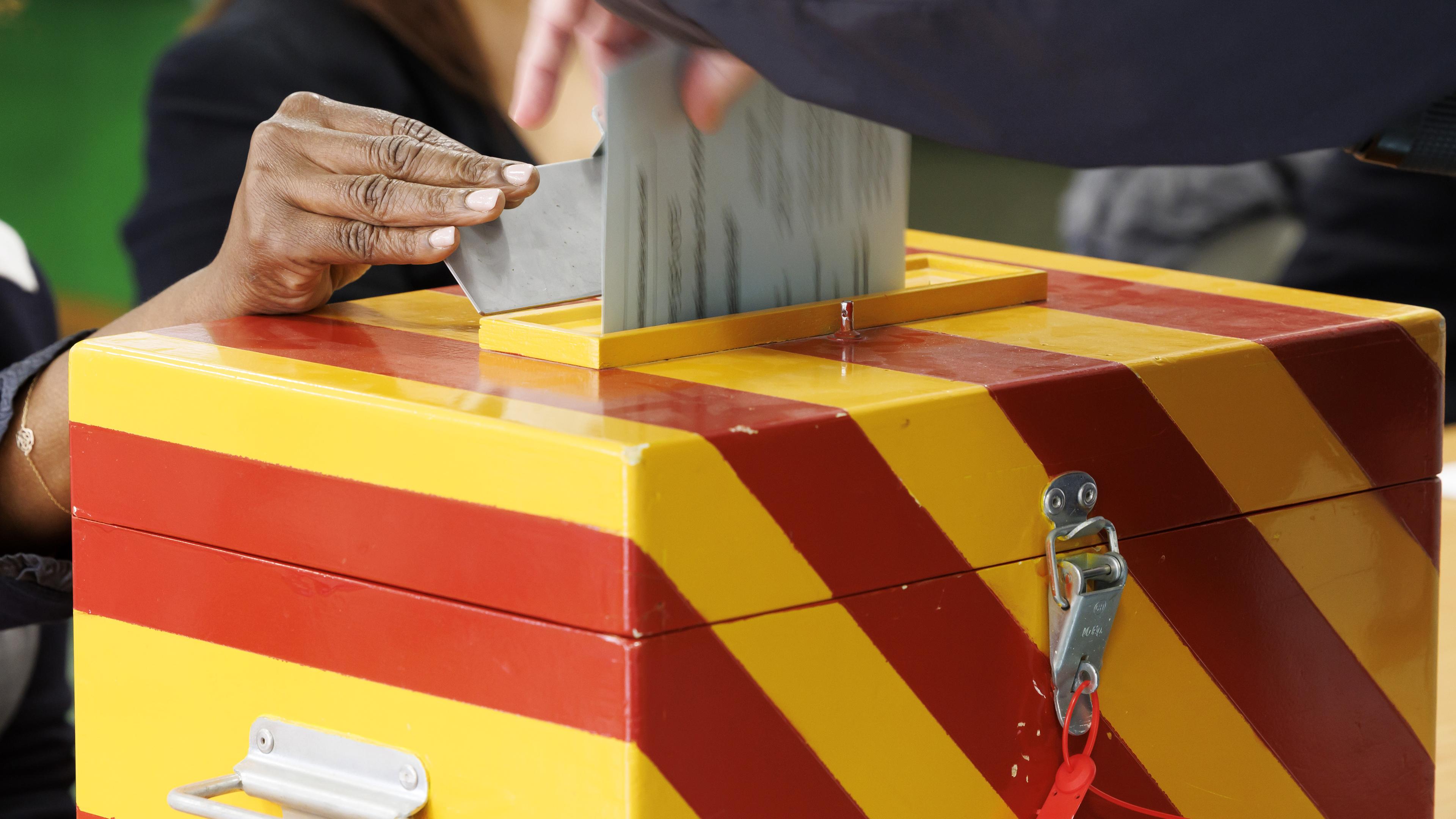 Schweiz, Meyrin: Stimmzettel für die Parlamentswahl werden von Wählern in die Wahlurne geworfen.