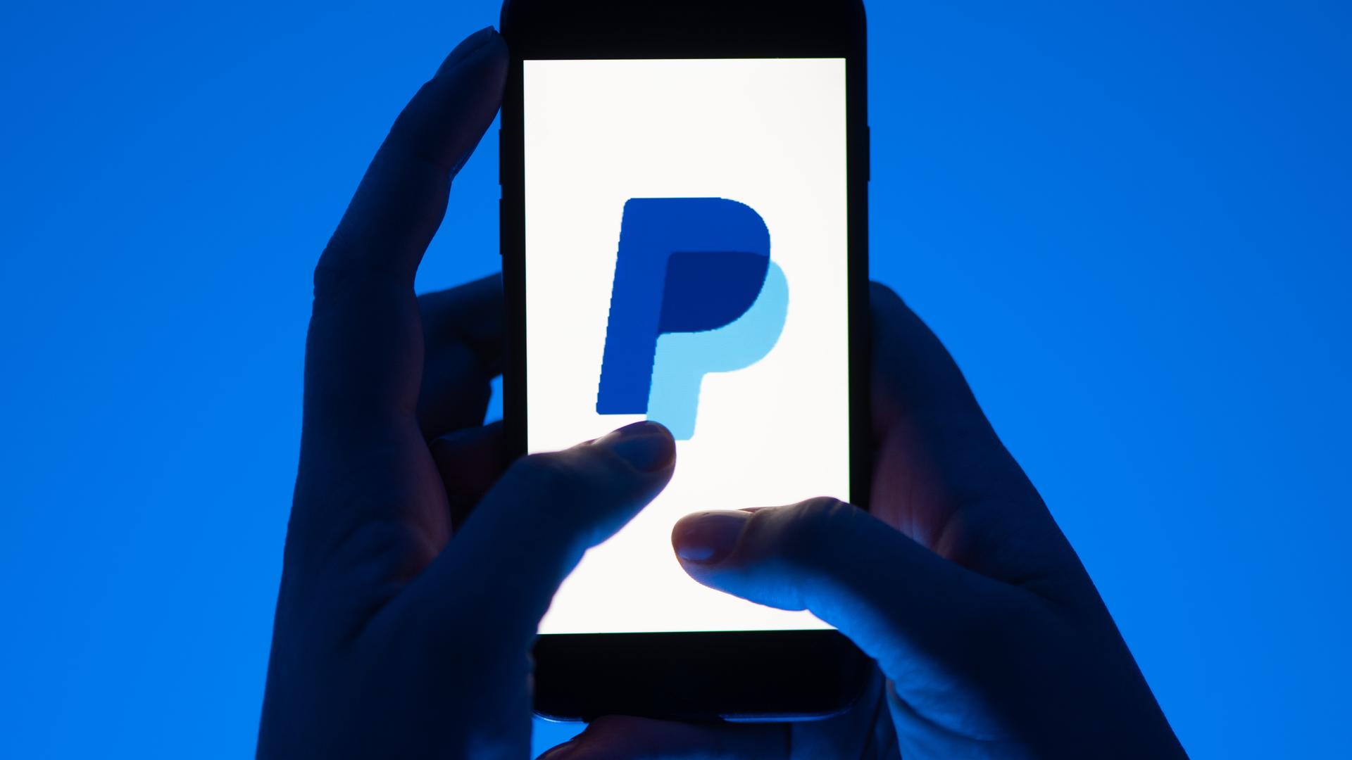 12.05.2022, Sachsen, Dresden: Eine Frau hält ein Smartphone mit dem Logo des Bezahldienst Paypal. (gestellte Szene)