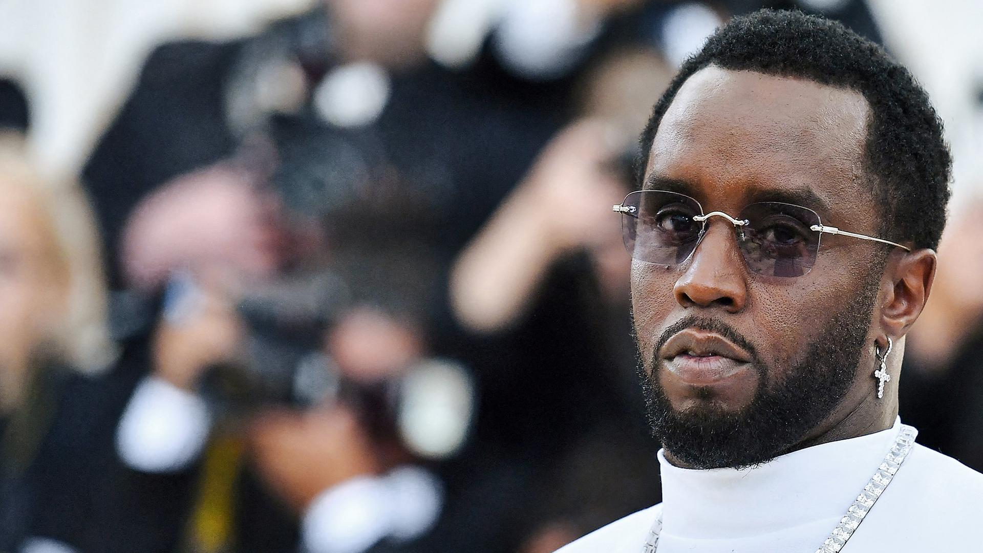 US-Rapper Sean Combs (P. Diddy) steht weiß gekleidet vor Kameras. 