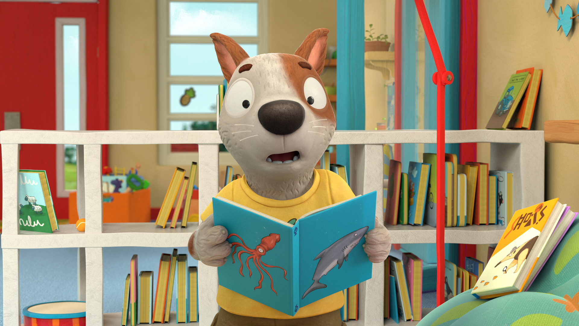 Zac hält ein Buch in den Pfoten und sieht geschockt aus. Auf dem Buch sind ein Krake und ein Hai abgebildet. Im Hintergrund steht ein Regal mit vielen Büchern.