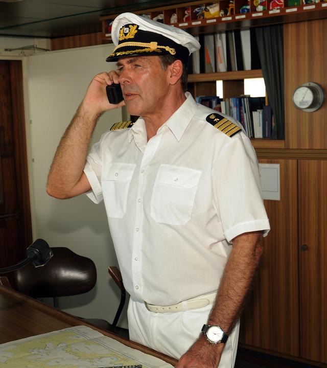 Kapitän Victor Burger (Sascha Hehn) steht telefonierend in Uniform auf der Brücke.