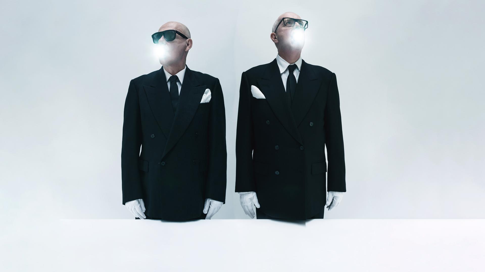 Die Pet Shop Boys stehen in Anzügen und Sonnenbrille vor der Kamera. Sie tragen weiße Handschuhe, aus ihrem Mund kommt weißes Licht.