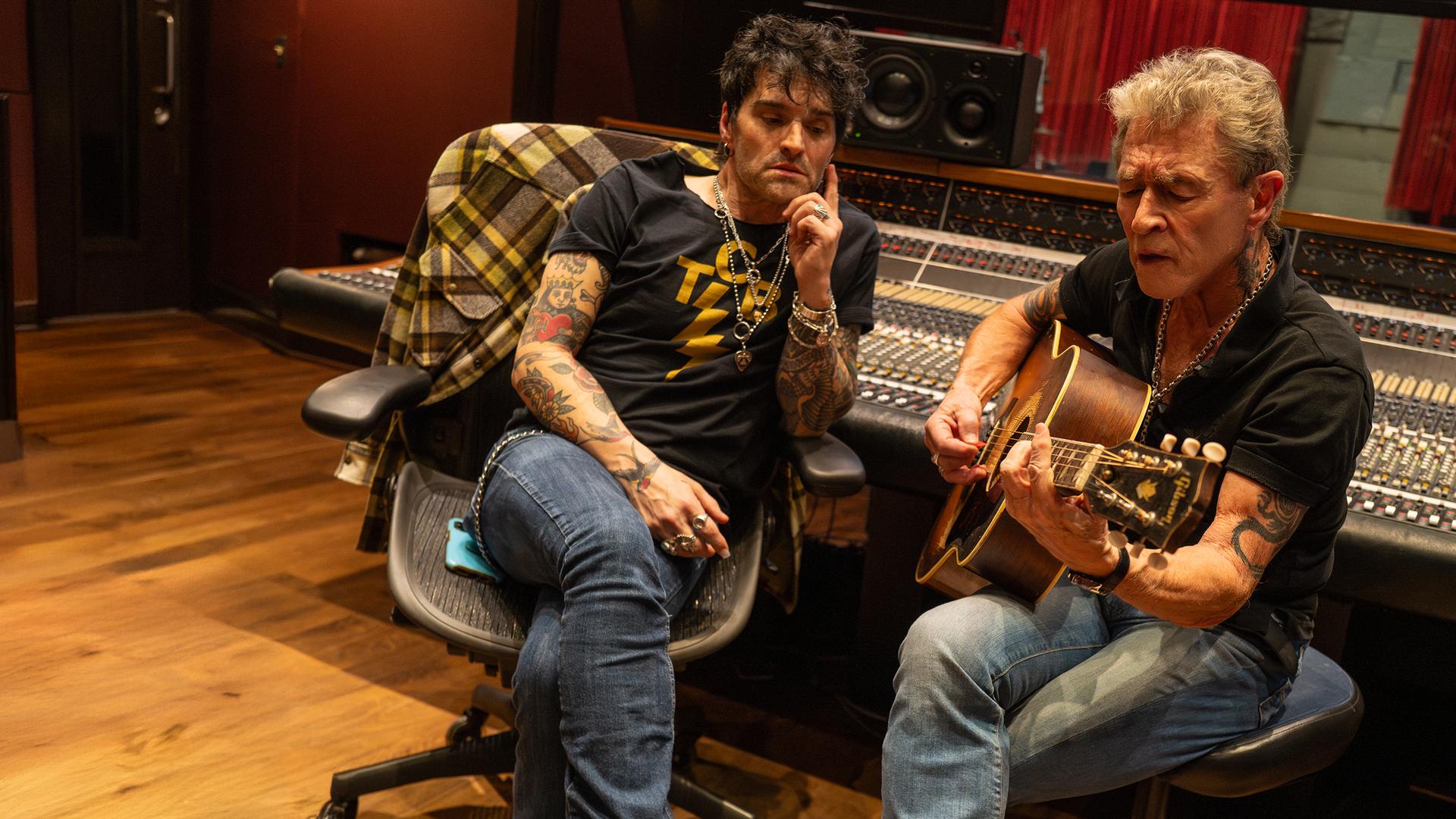 Peter Maffay sitzt auf einem Stuhl, spielt Gitarre und singt. Hinter ihm ist ein großes Mischpult und neben ihm sitzt ein Mann, der Peter Maffay anschaut.