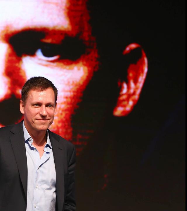 Ein Mann läuft vor einem riesigen an die Wand projizierten Fotos seines eigenen Gesichts.