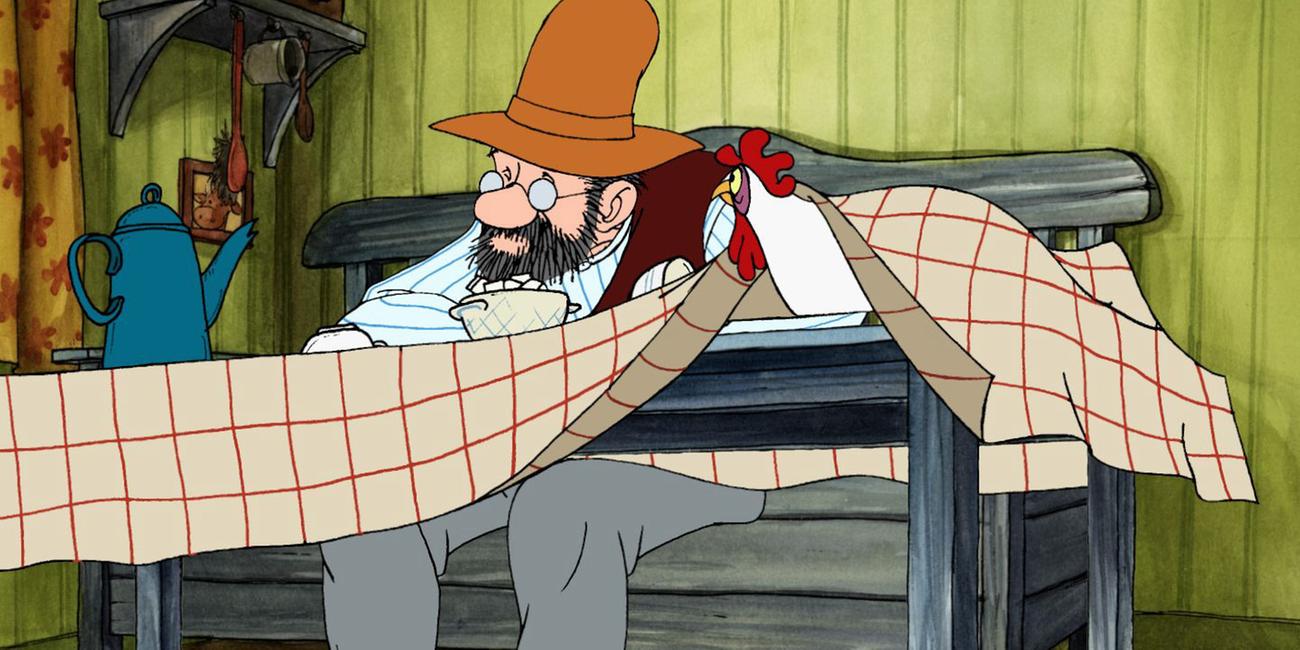 Pettersson sitzt deprimiert am Esstisch in der Küche. Ein Huhn, das unter der Tischdecke sitzt, schaut ihn an.