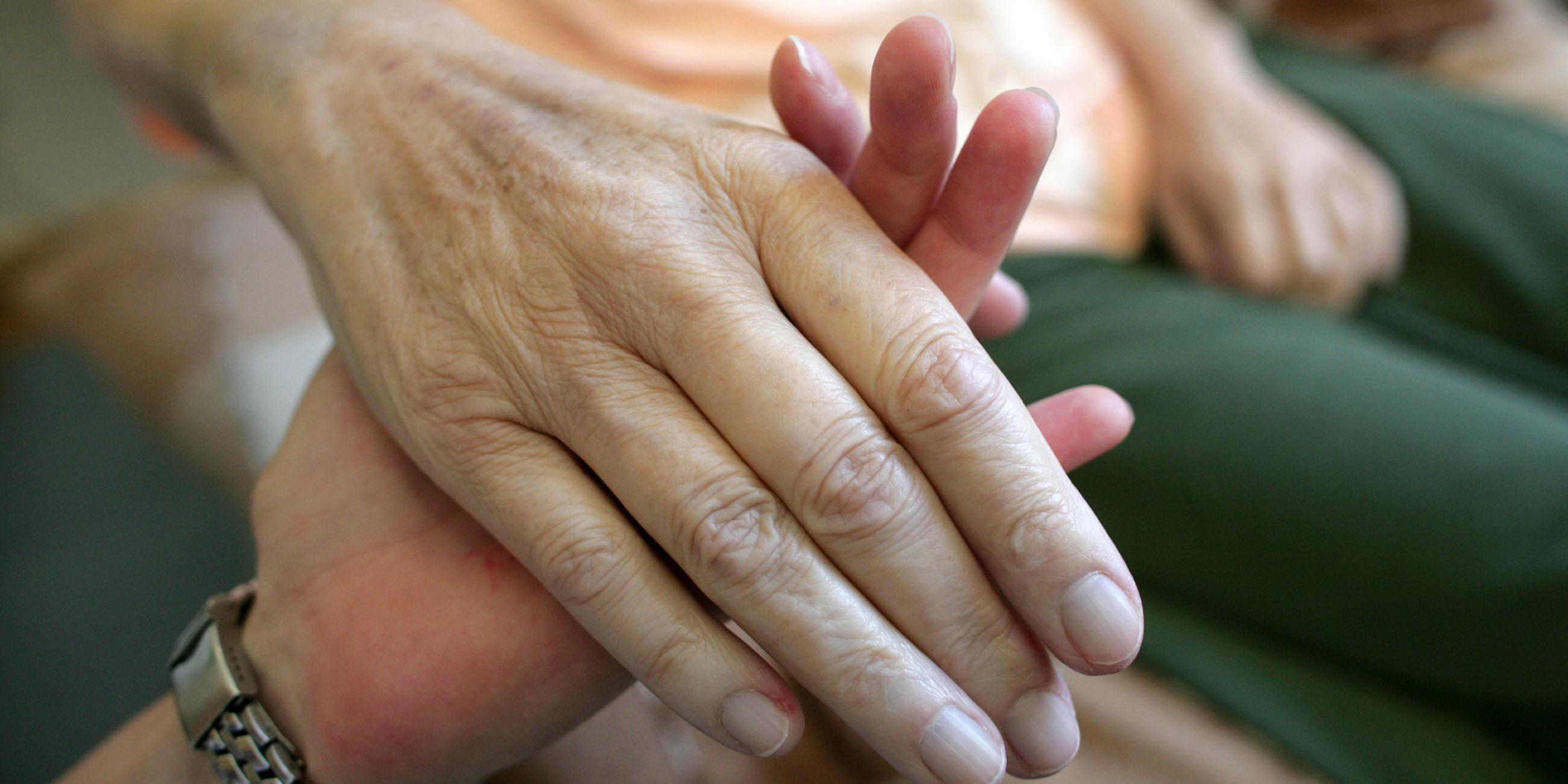 Die Hand einer alten Frau wird von einer pflegenden Person gehalten.