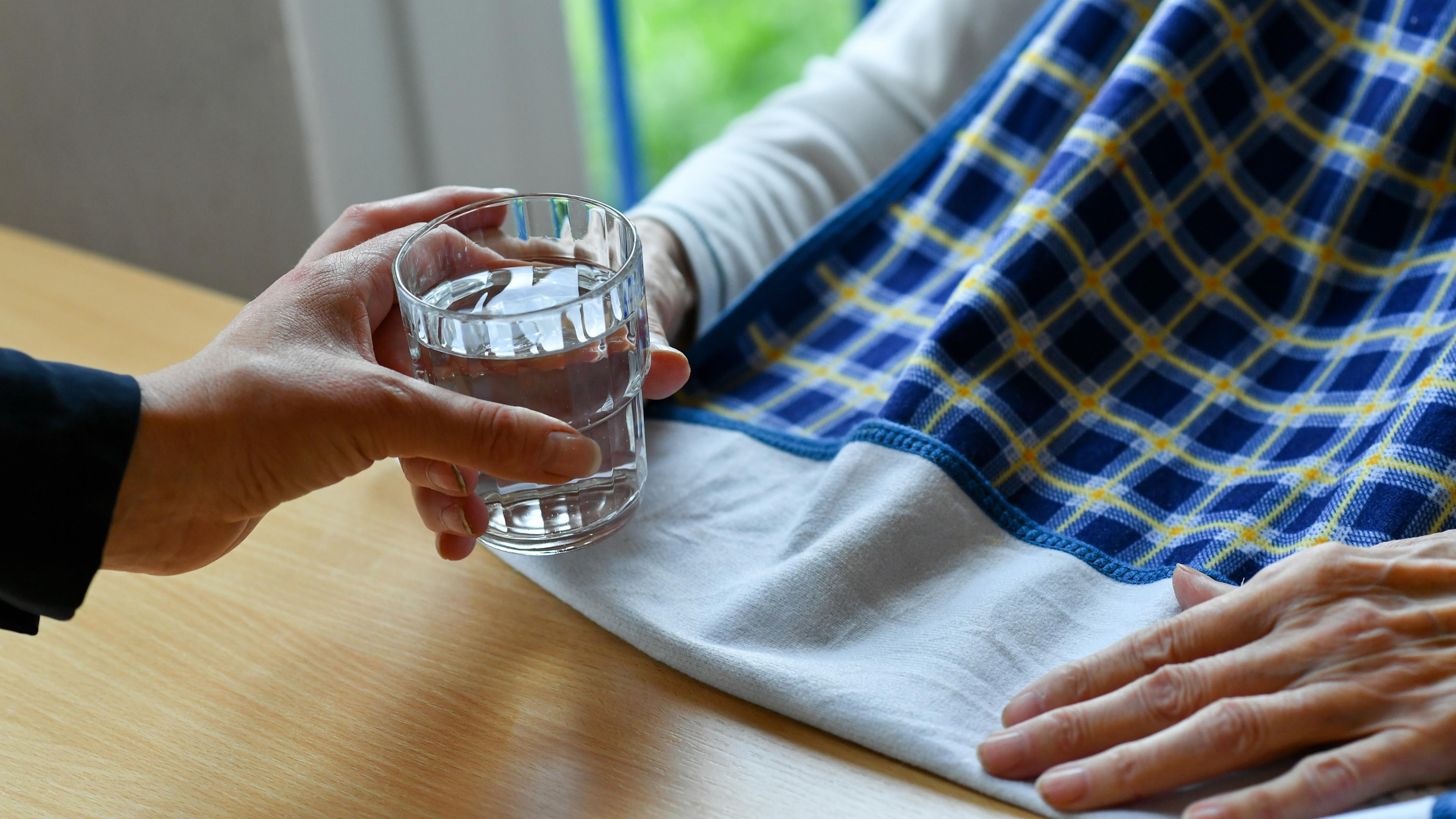 Eine Pflegerin reicht einer alten Frau ein Glas Wasser.