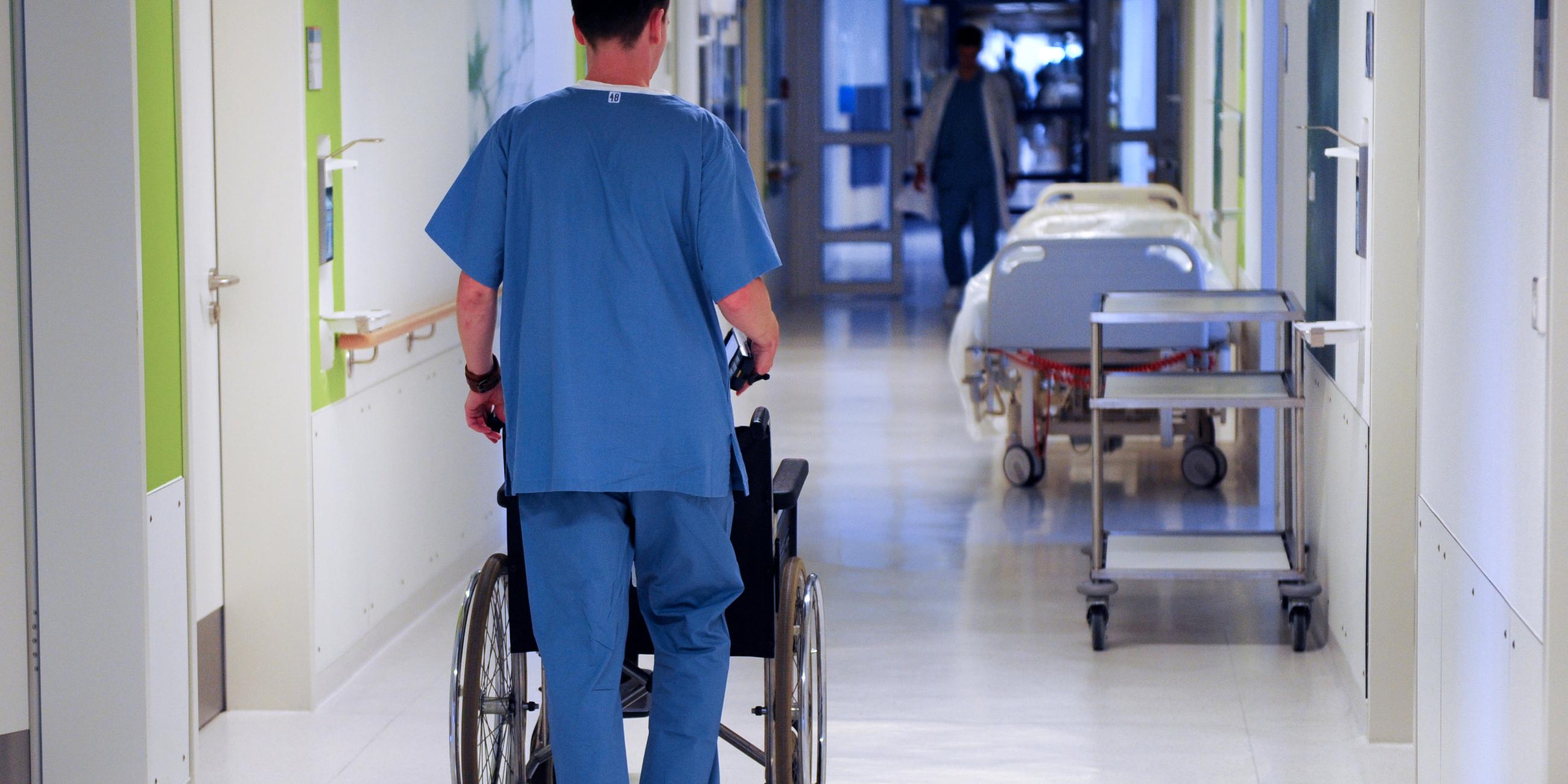 Archiv: Ein Pfleger schiebt einen Rollstuhl über einen Krankenhausflur