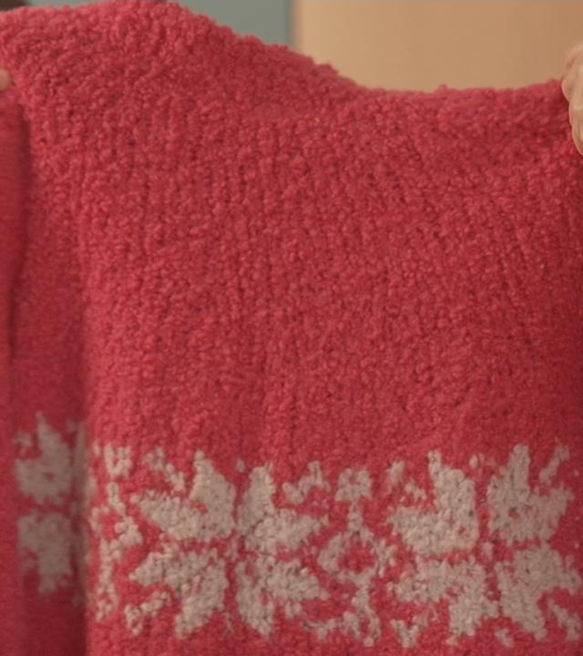 Ein roter Wollpulli wird ins Bild gehalten.