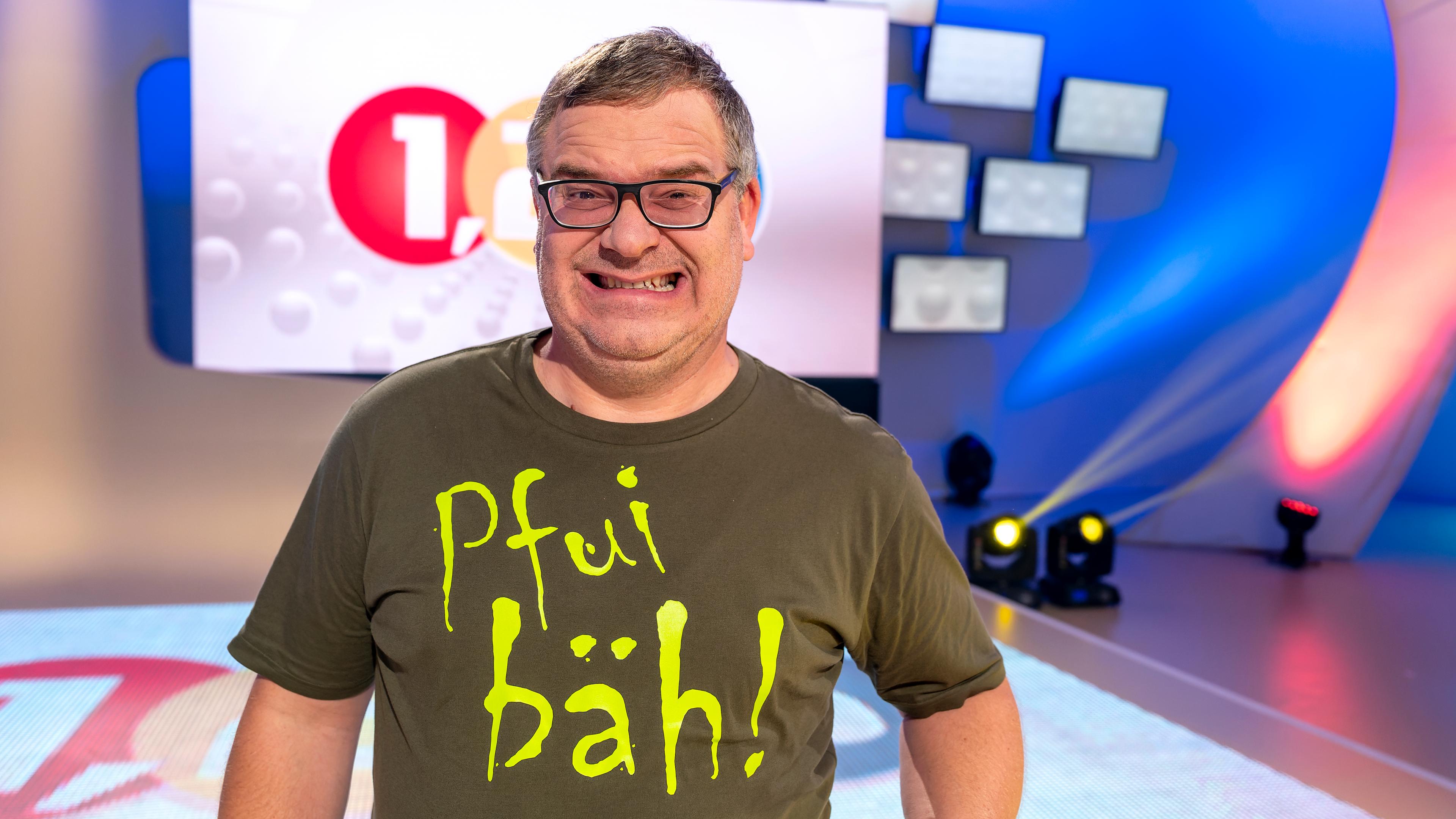 1, 2 oder 3: Moderator Elton steht vor der Vidiwall im 1, 2 oder 3-Studio und trägt ein Tshirt mit dem Schriftzug "Pfui bäh".