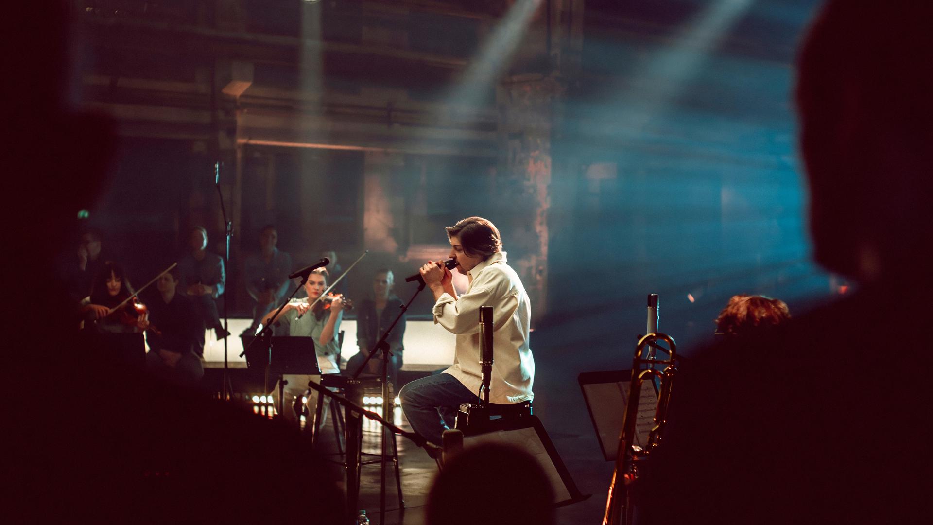 Der Sänger Philipp Poisel sitzt auf der Bühne und singt in ein Mikro.