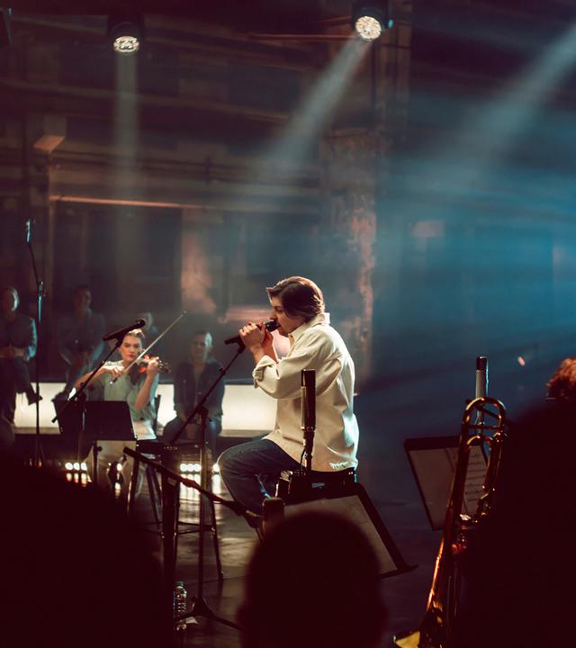 Der Sänger Philipp Poisel sitzt auf der Bühne und singt in ein Mikro.