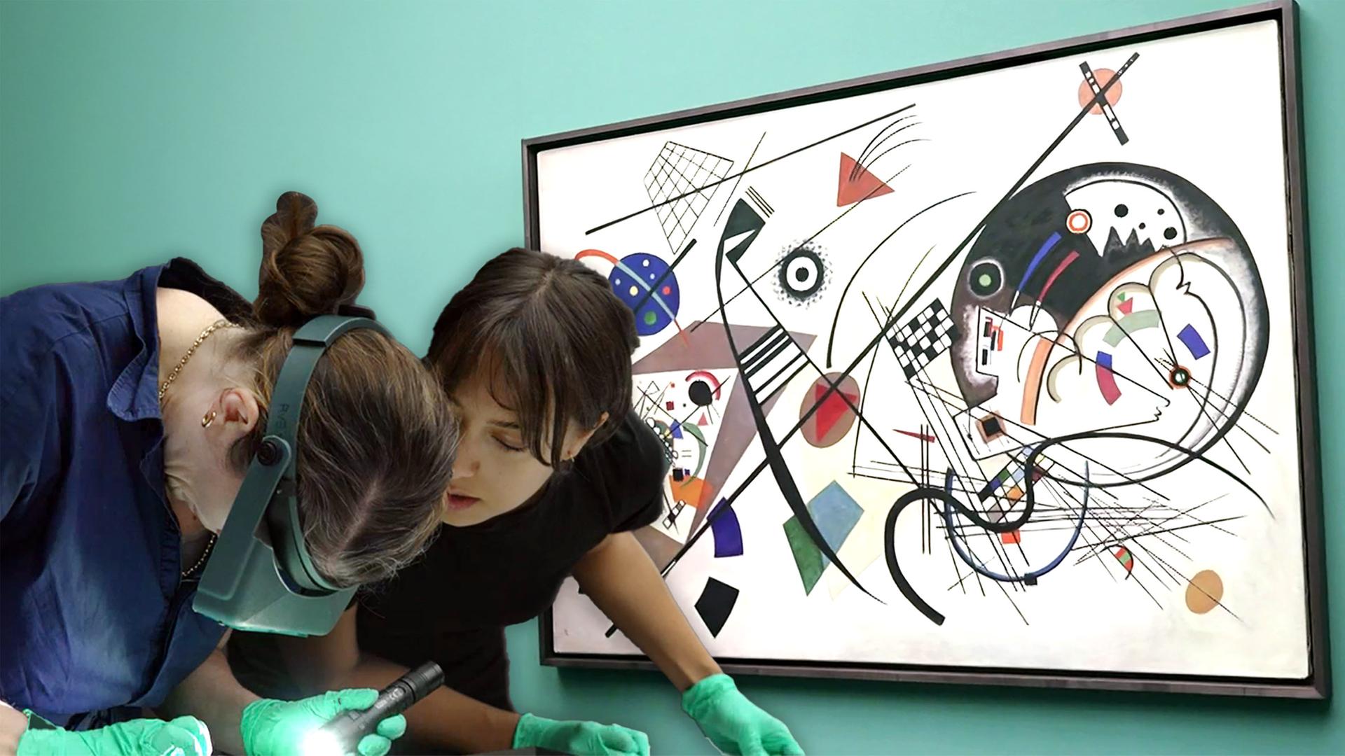 Zwei Frauen beugen sich neben einem an der Wand hängenden Bild von Miró auf ein vor ihnen liegendes Werk.