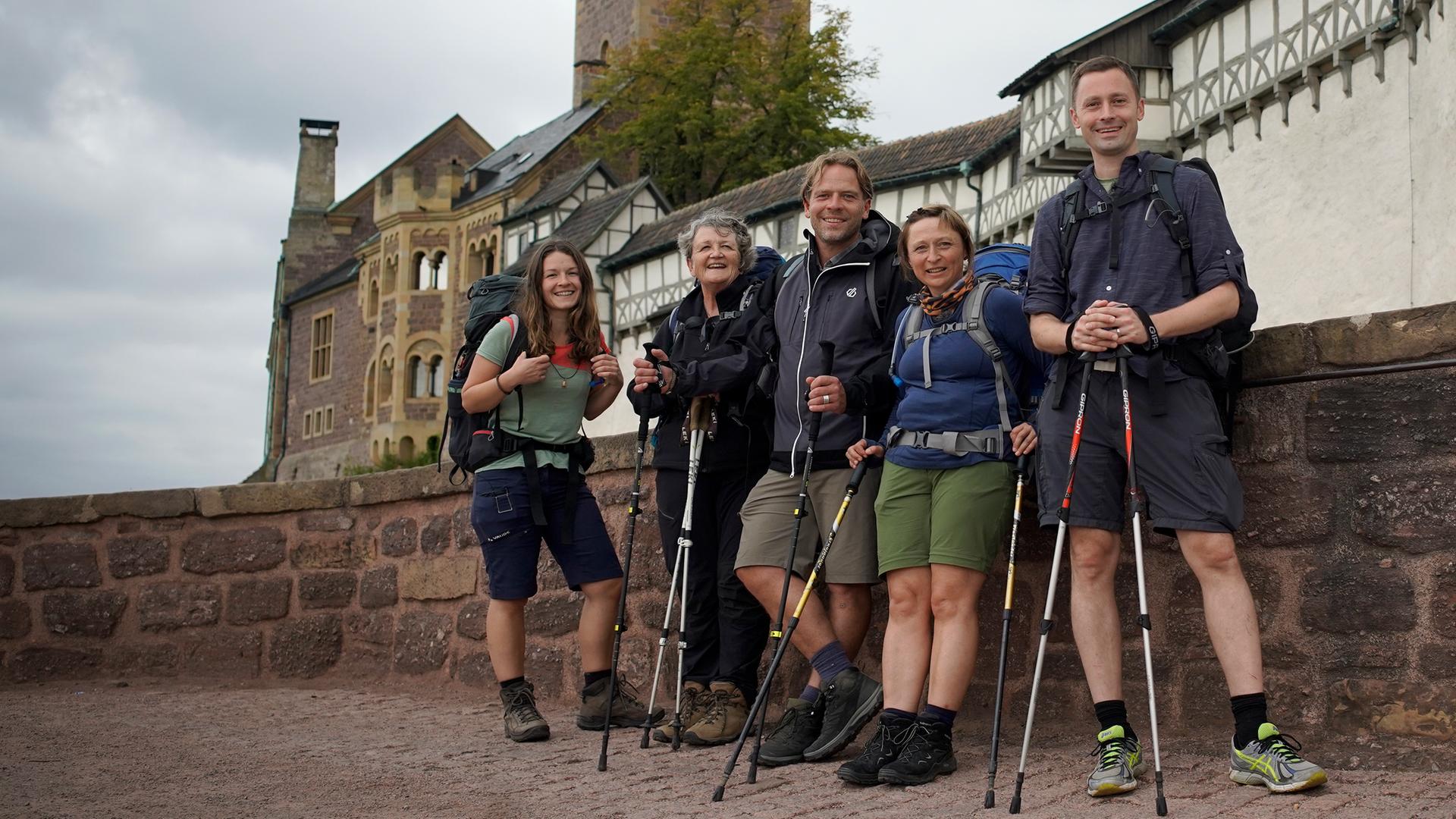 Fünf Pilger stehen mit Outdoorkleidung und Rucksäcken vor der Wartburg und schauen in die Kamera.