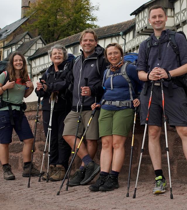 Fünf Pilger stehen mit Outdoorkleidung und Rucksäcken vor der Wartburg und schauen in die Kamera.