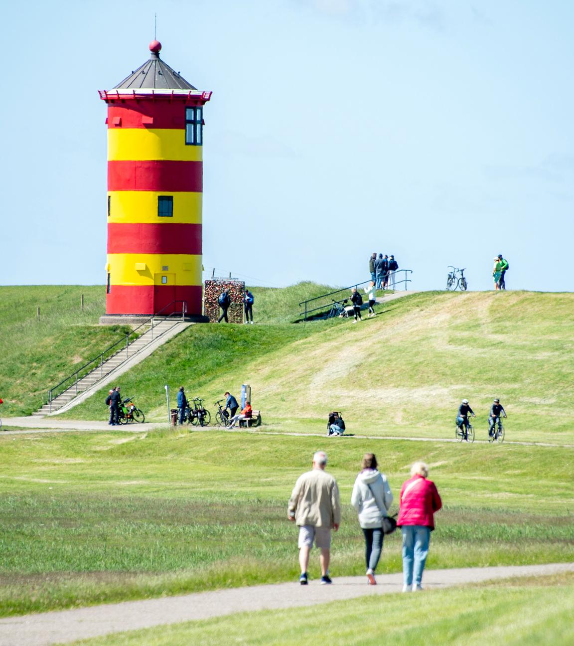 Niedersachsen, Pilsum: Touristen gehen auf dem Deich vor dem Pilsumer Leuchtturm spazieren.