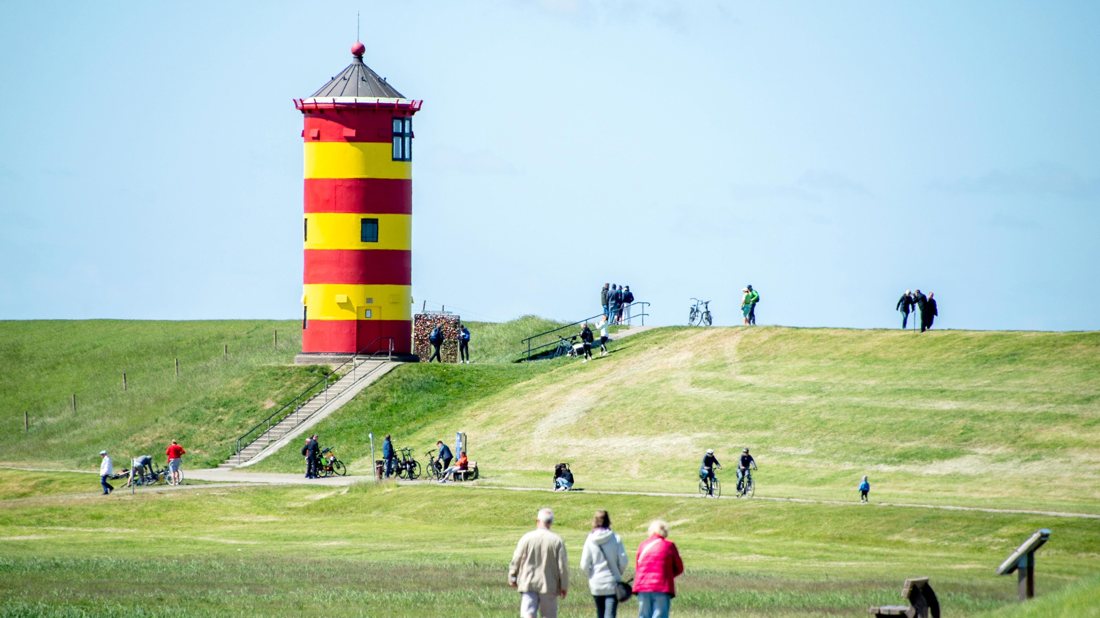 Niedersachsen, Pilsum: Touristen gehen auf dem Deich vor dem Pilsumer Leuchtturm spazieren.