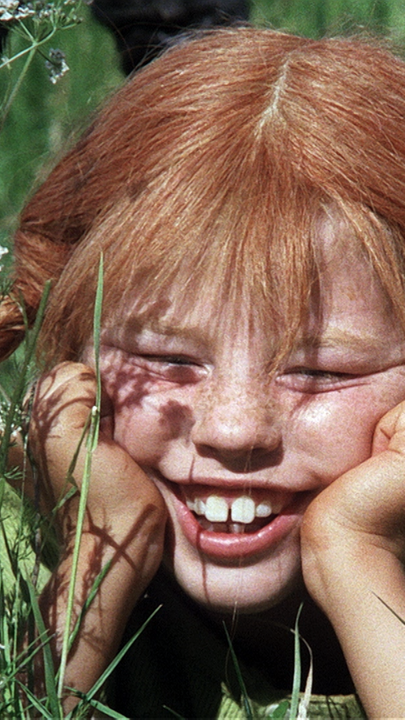 Pippi Langstrumpf (Mitte) liegt im Gras und stützt ihr Gesicht auf ihren Händen ab.